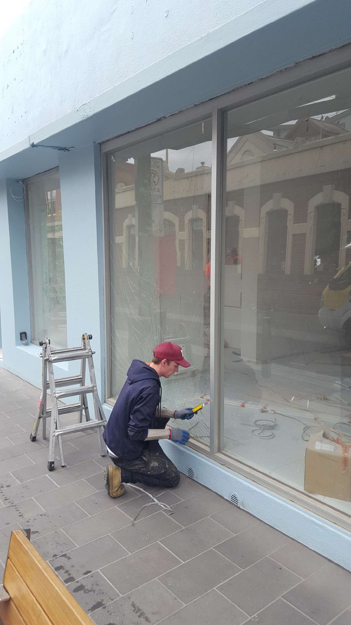A man is kneeling down in front of a building cleaning a window.