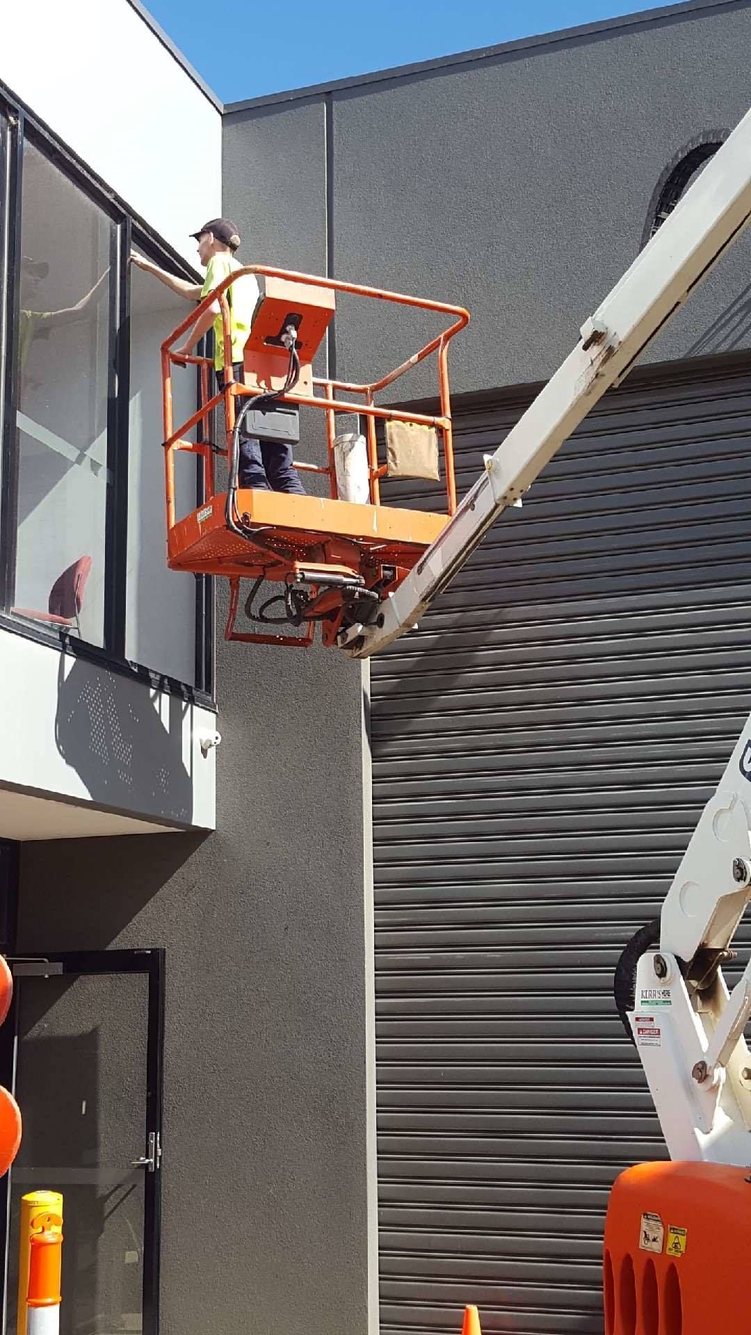 A man is standing on a lift in front of a building.