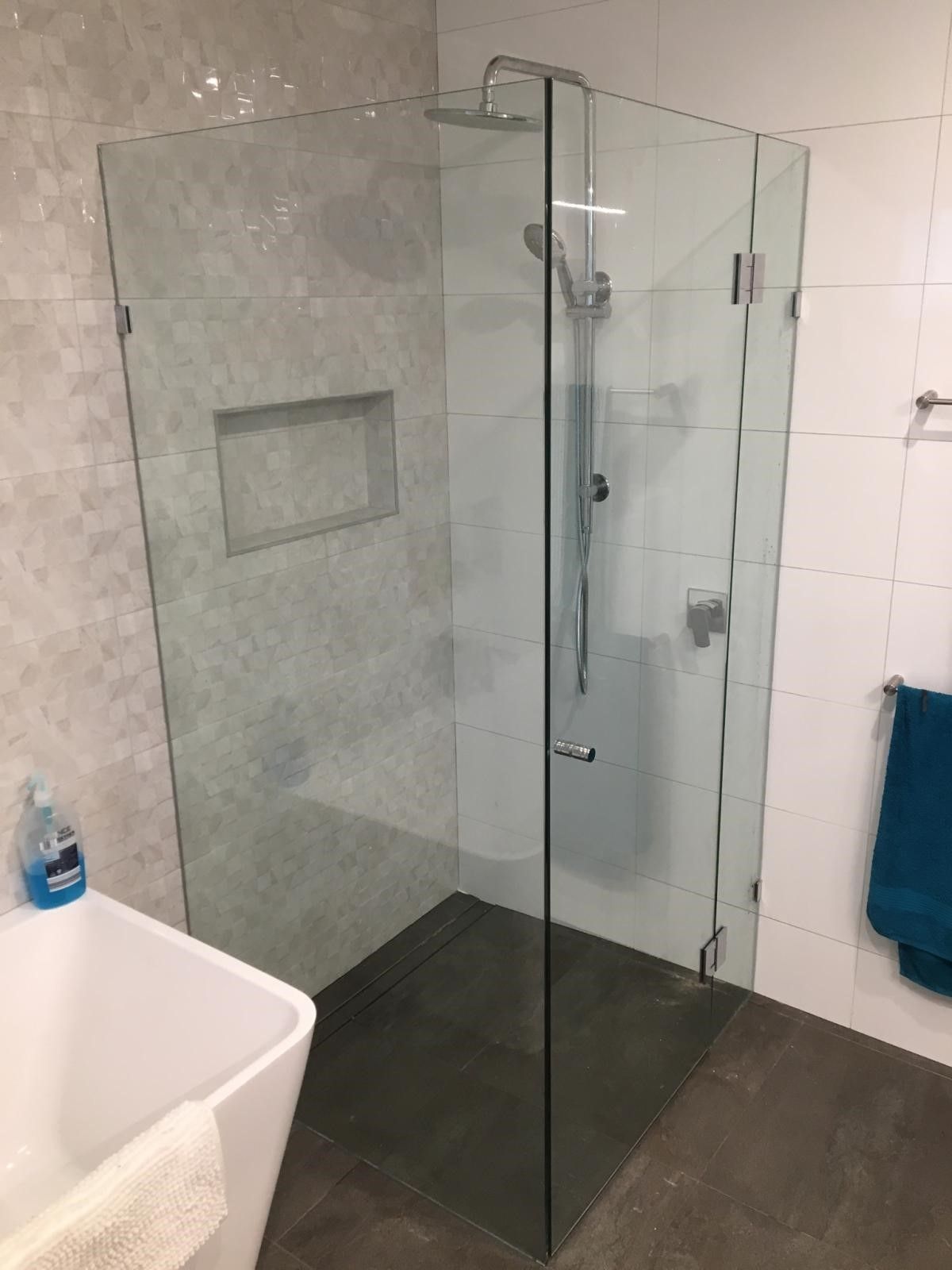 Glass shower enclosure in modern bathroom with tiled walls and dark floor.