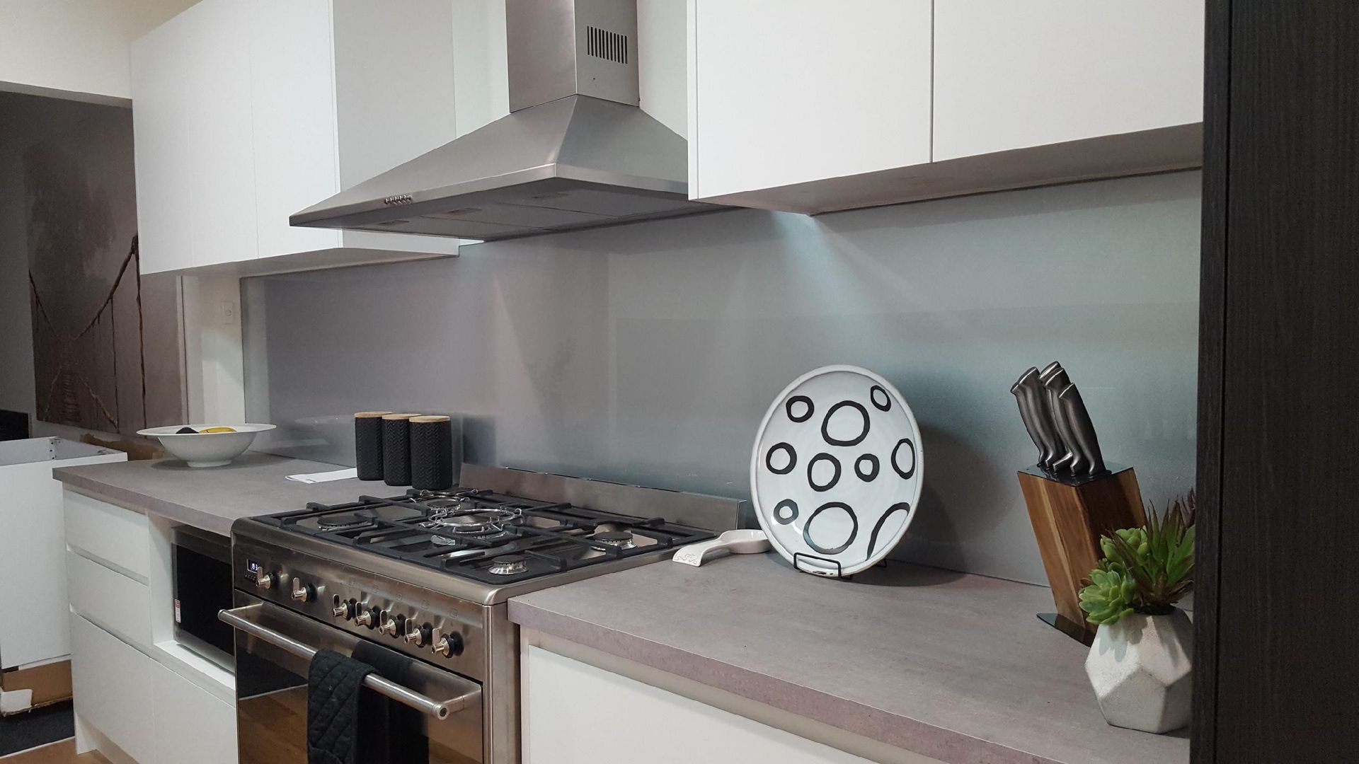 Kitchen with stainless steel range, white cabinets, and a plate with black circles on the counter.