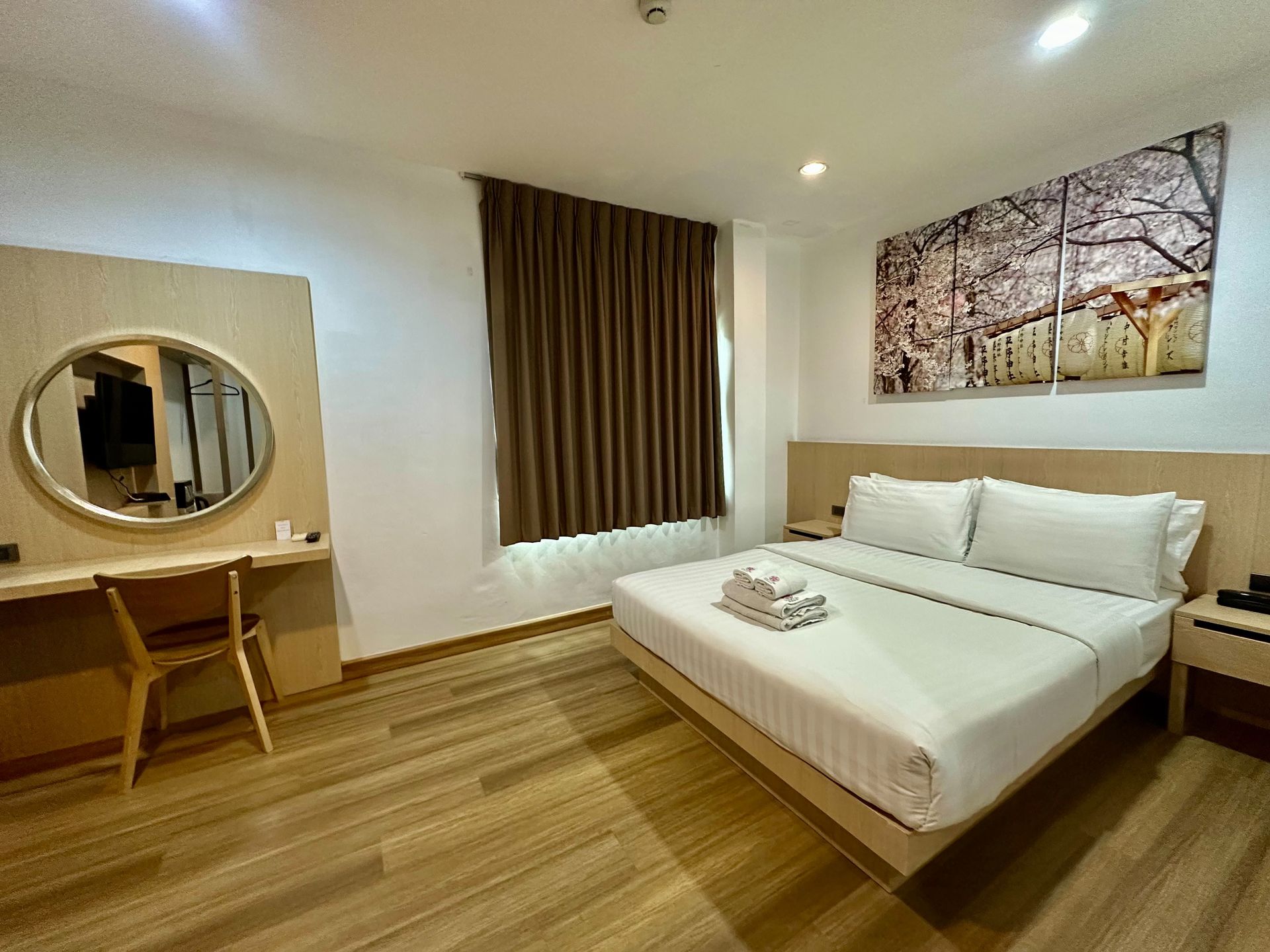 Hotel room with a bed, desk with mirror, and window with brown curtains.