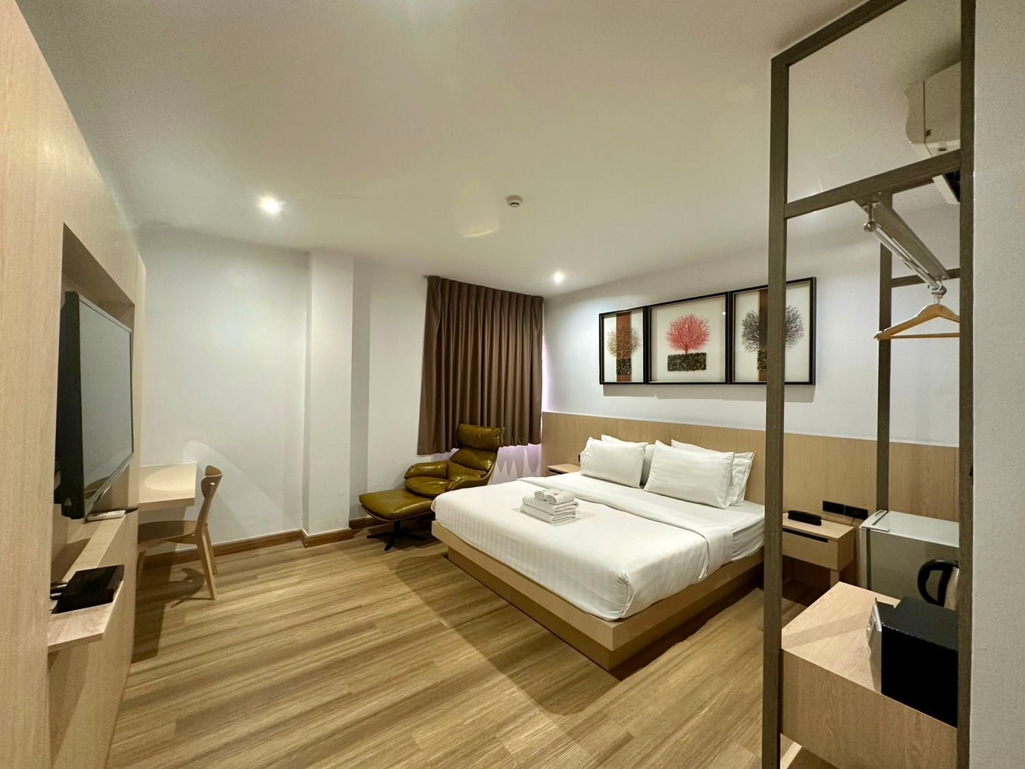 Hotel room interior with a bed, desk, chair, closet, and artwork.