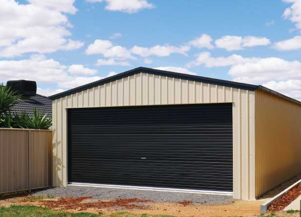 Detached beige garage with a large black roller door under a partly cloudy sky