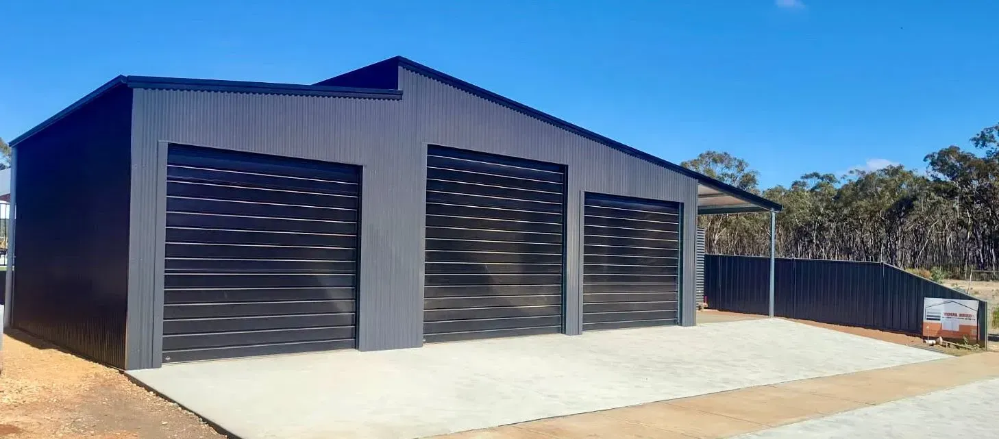 Modern industrial shed with three black roller doors and a concrete apron under a blue sky