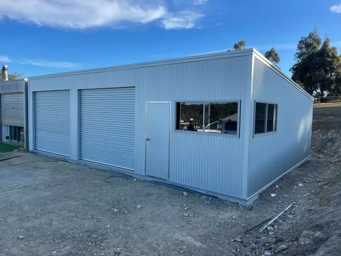 Blue metal shed in a grassy rural yard under a partly cloudy sky