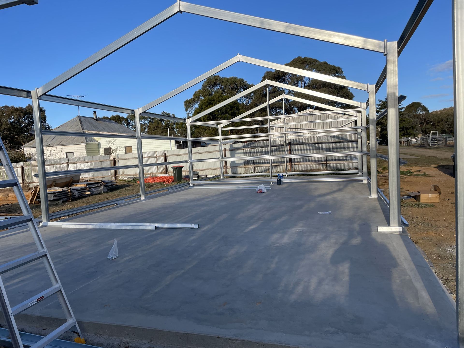 Steel frame building under construction with a concrete slab and ladder in the foreground.