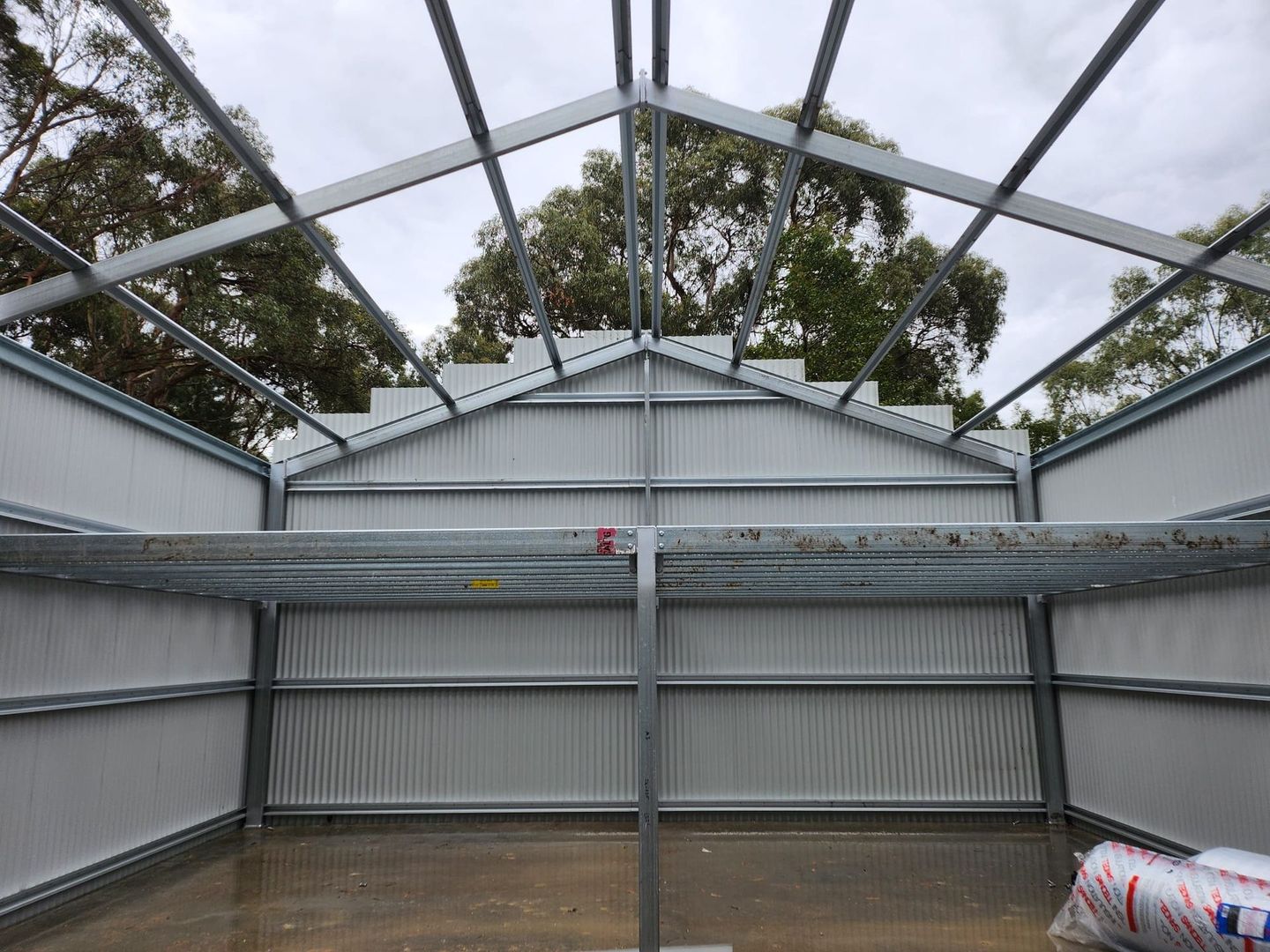 Indoor construction area with corrugated metal walls, exposed roof beams, and stacked materials on the floor