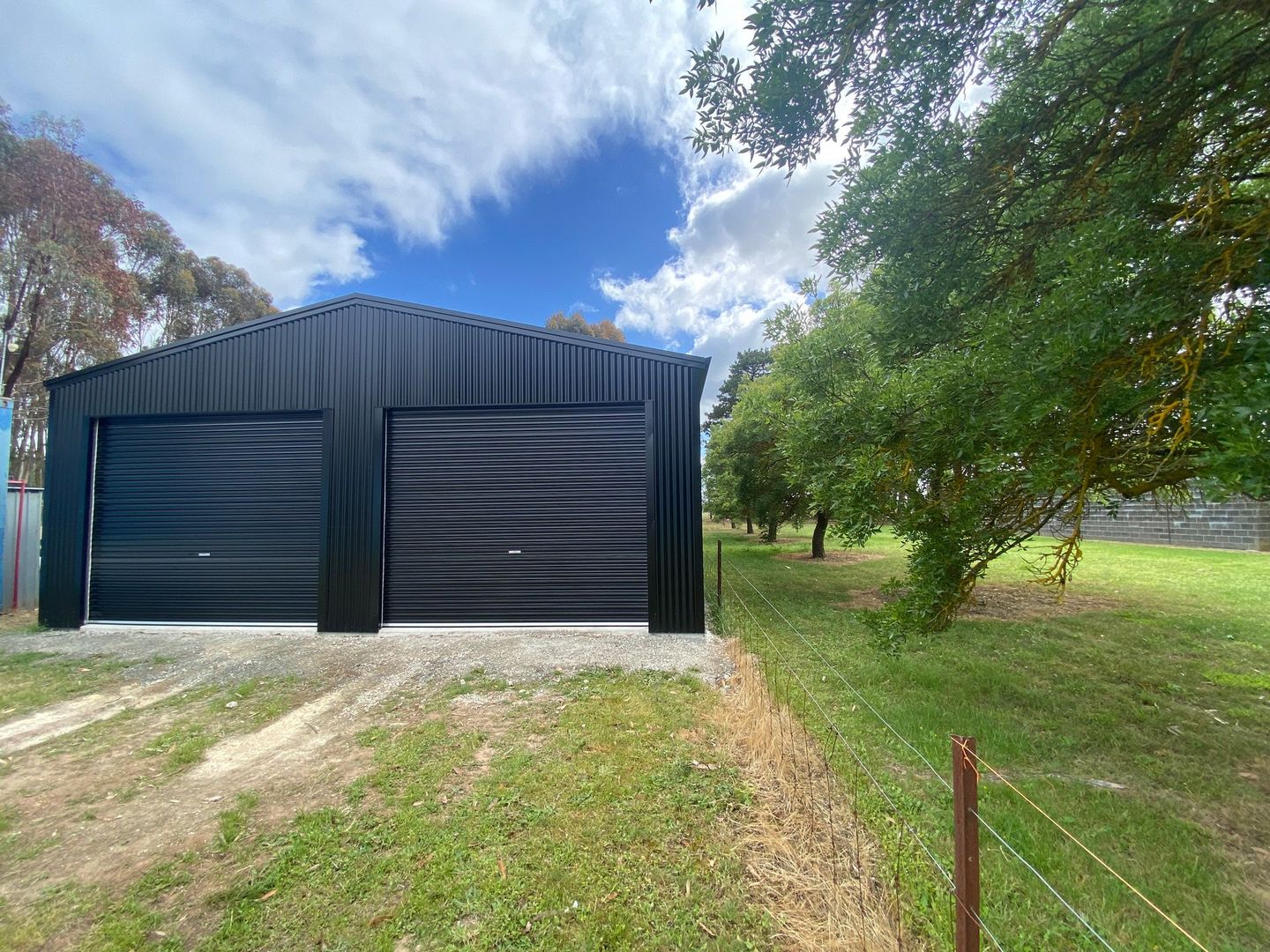 Black metal garage with two doors beside a grassy yard under a cloudy blue sky