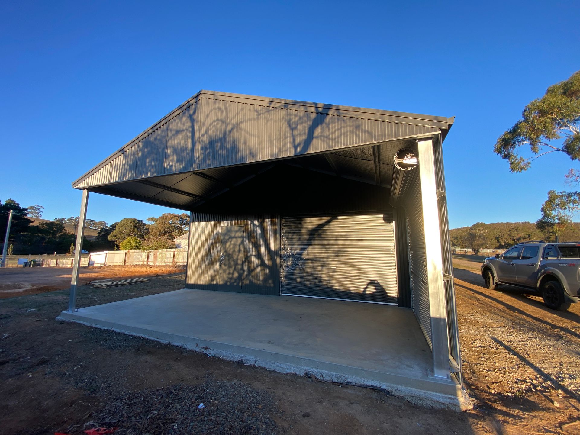 Open-sided concrete bus shelter with metal roof on a sunny roadside, cars parked nearby