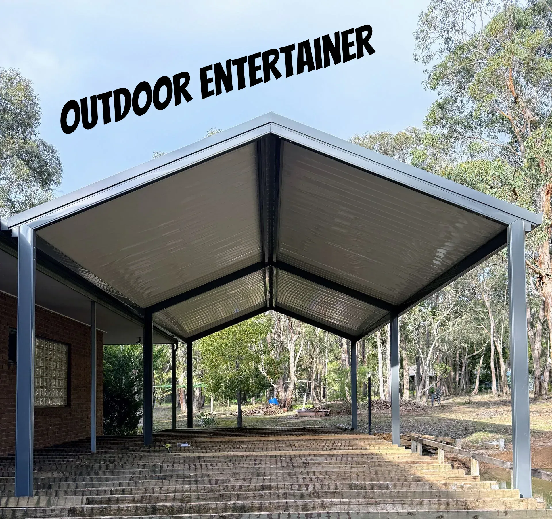 Covered outdoor patio with metal roof and open sides under trees, labeled “OUTDOOR ENTERTAINER”