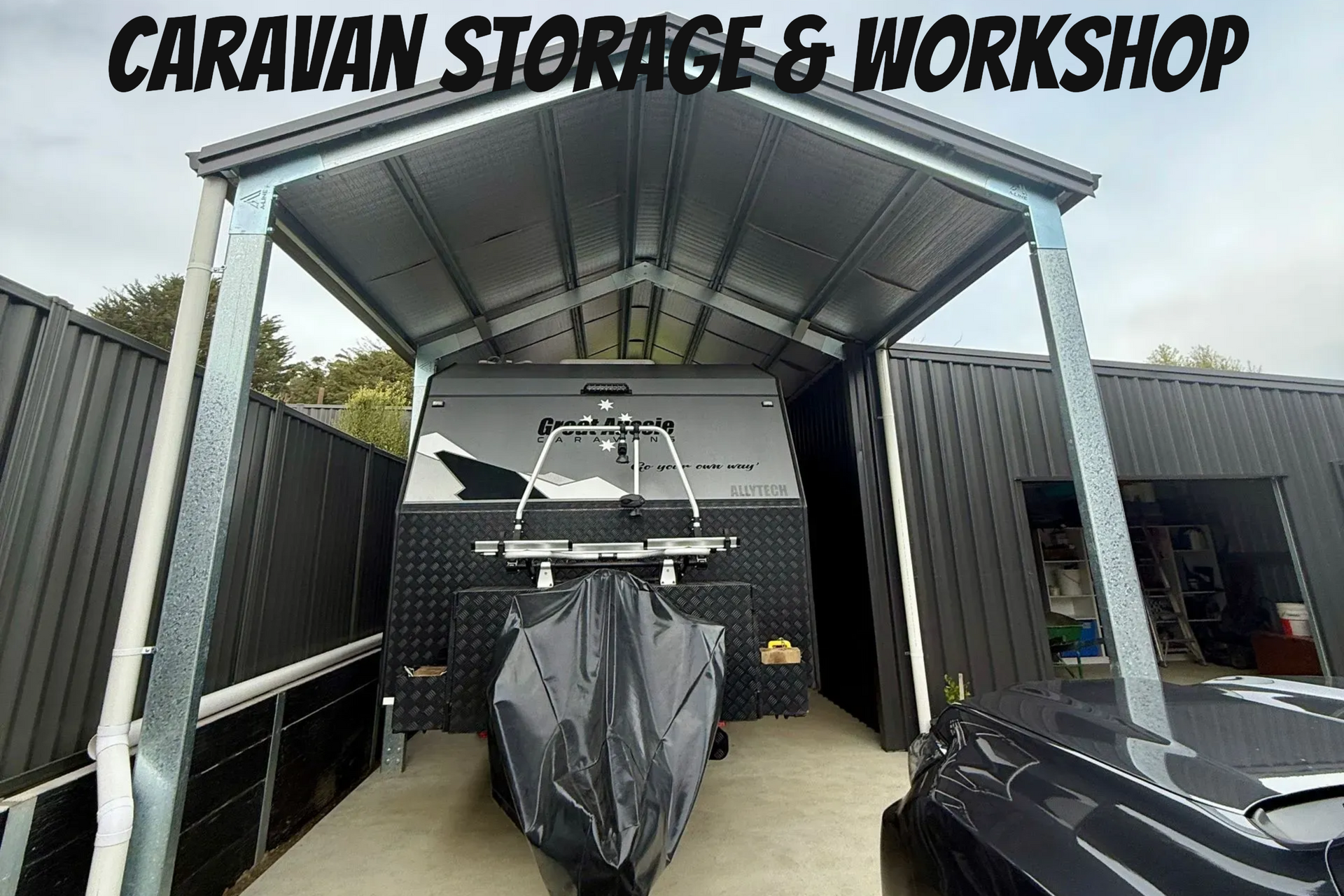 Covered caravan workshop with a boat trailer centered under a metal roof, black vehicle at right.