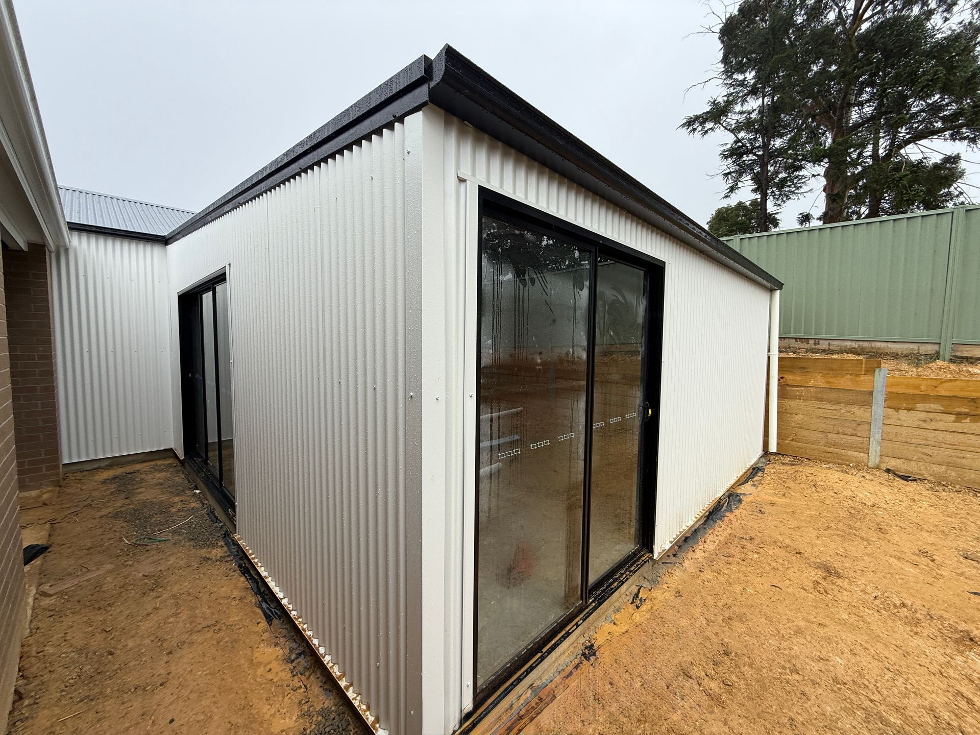Small metal outbuilding with sliding glass doors beside a yard and fence