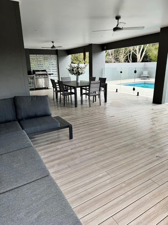 Covered patio with gray sectional, dining table, ceiling fans, and a pool in the background.