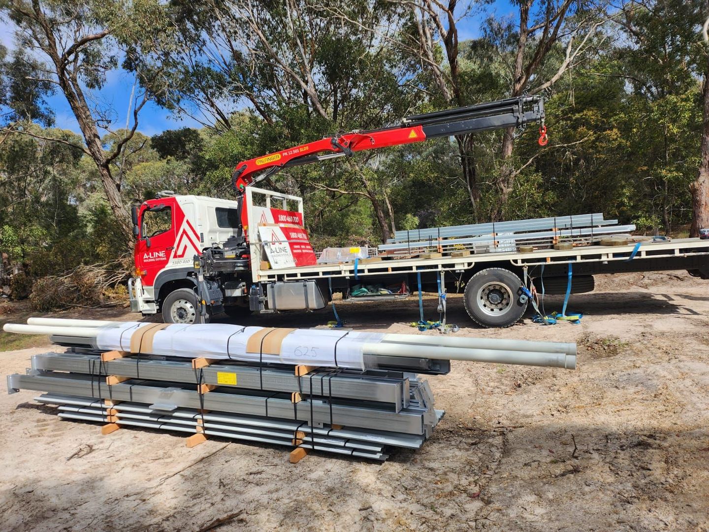 Truck-mounted crane lifting metal pipes at a construction site, with stacked pipes in the foreground.