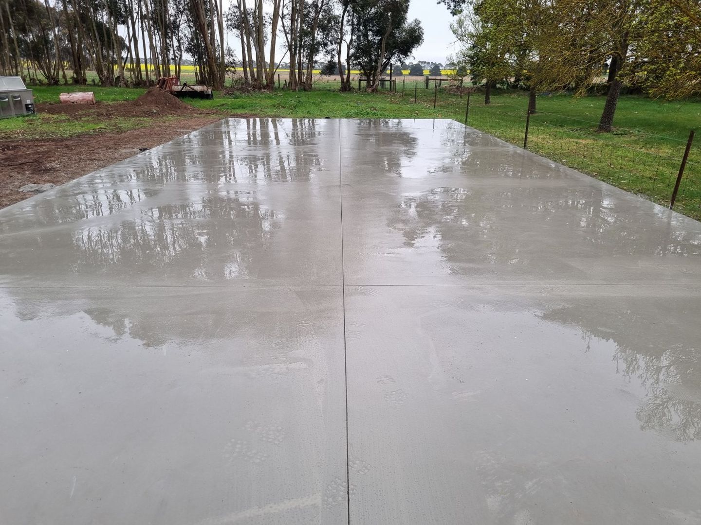 Wet concrete driveway reflecting trees in a rainy park-like setting