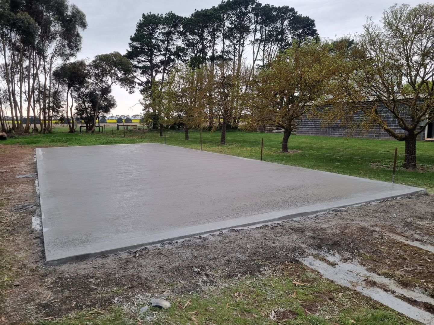 Freshly poured concrete slab in a grassy park with trees and a dirt edge