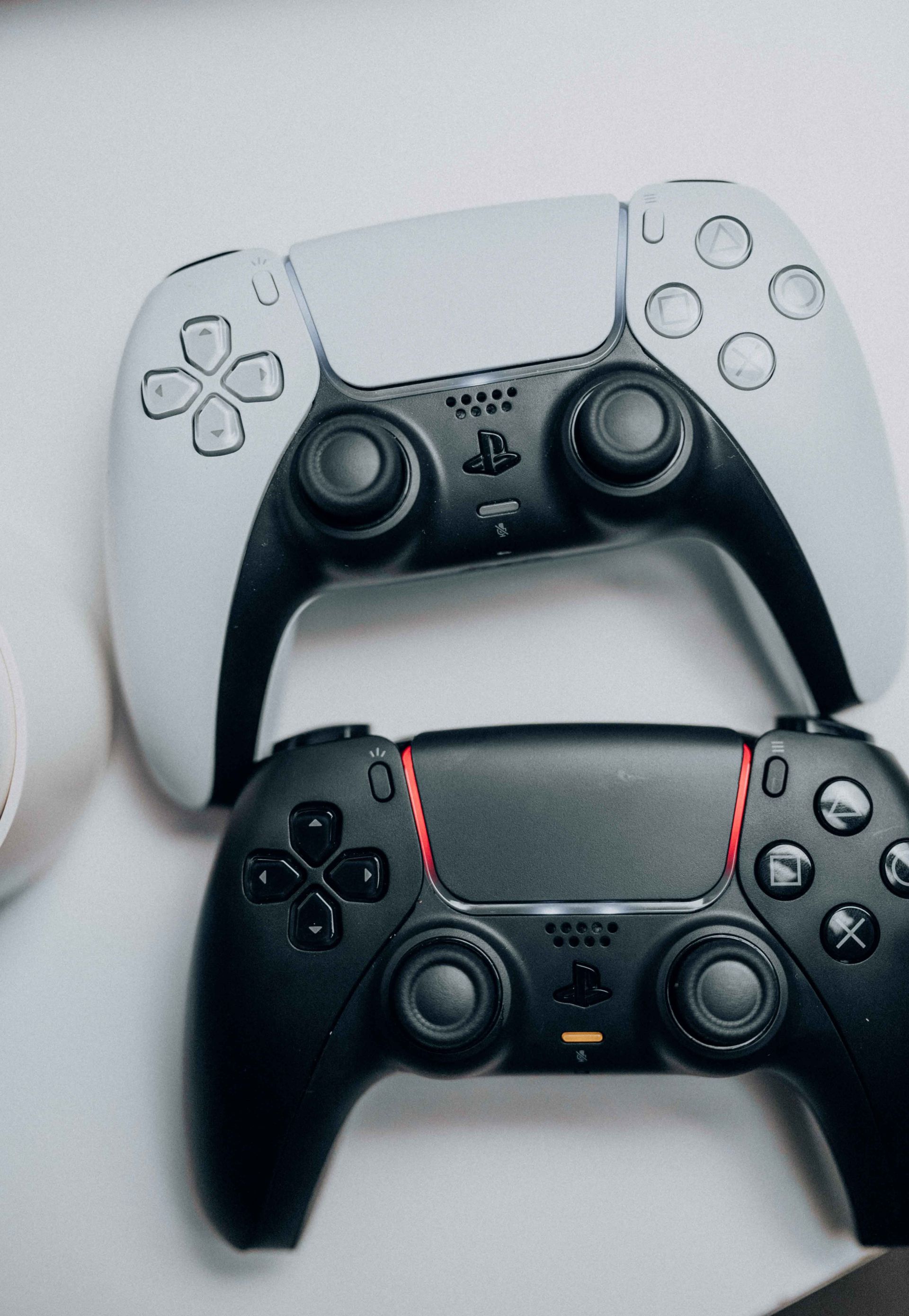 Dos mandos de videojuegos estilo PlayStation, uno blanco y otro negro, apilados sobre una superficie clara.