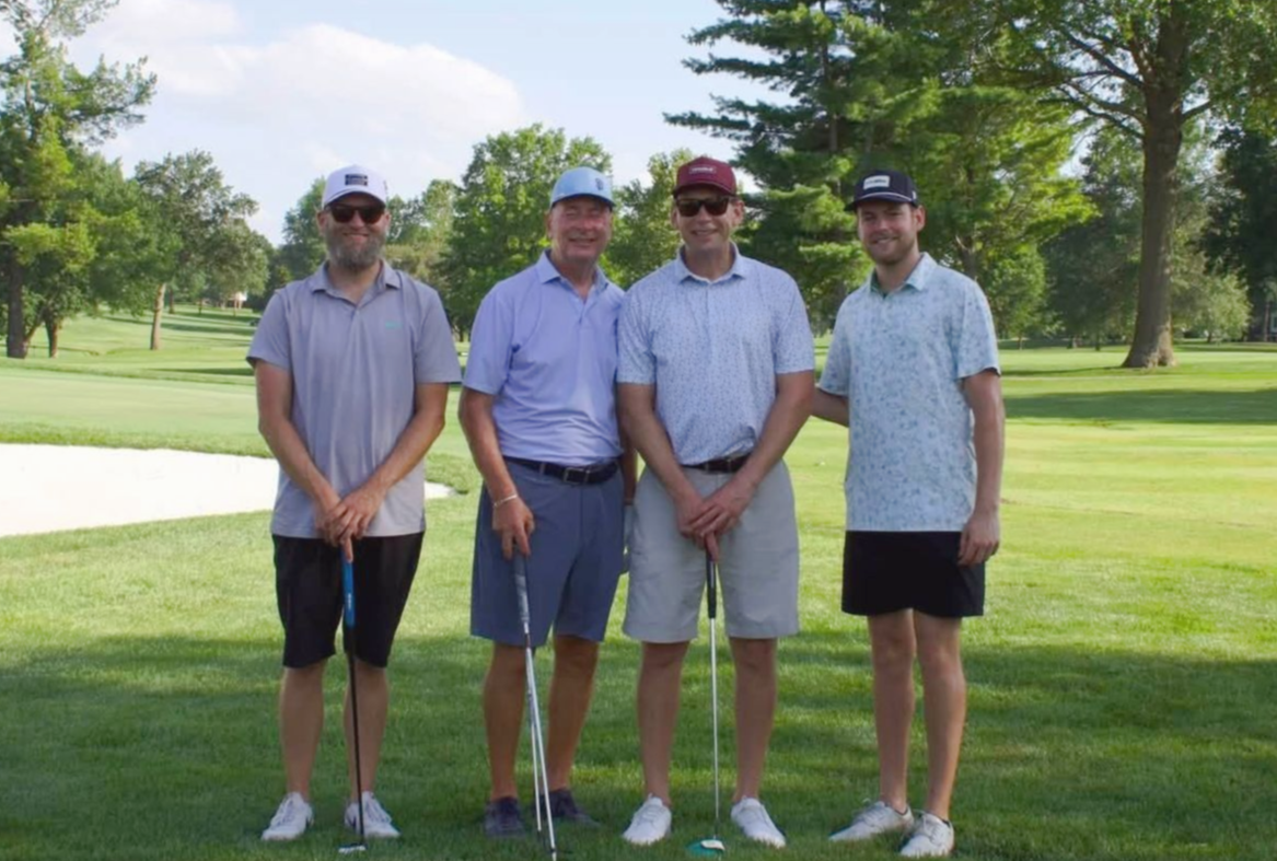 Four men are posing for a picture in front of a sign that says valley school district