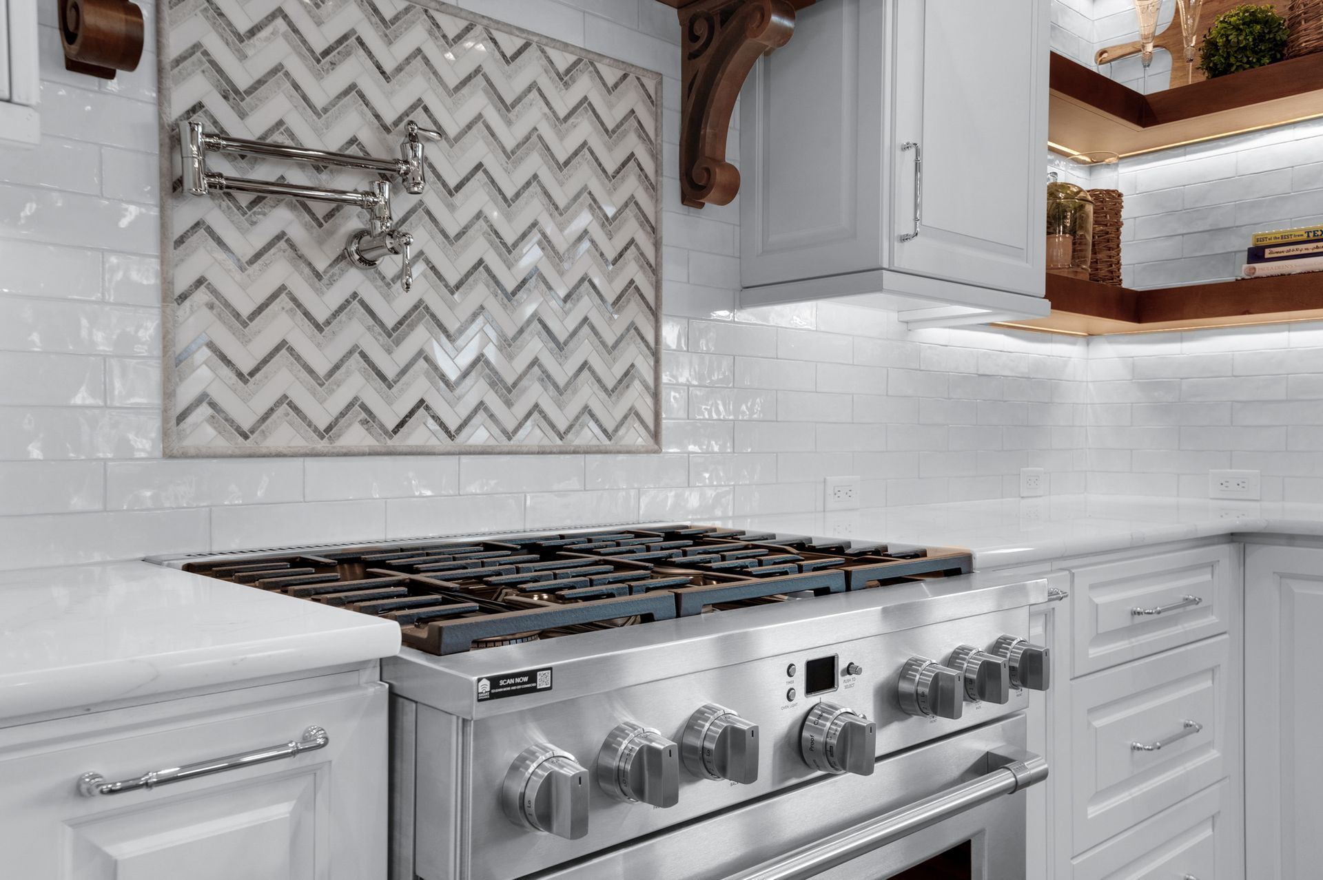 Stainless steel range in white kitchen with chevron tile backsplash.