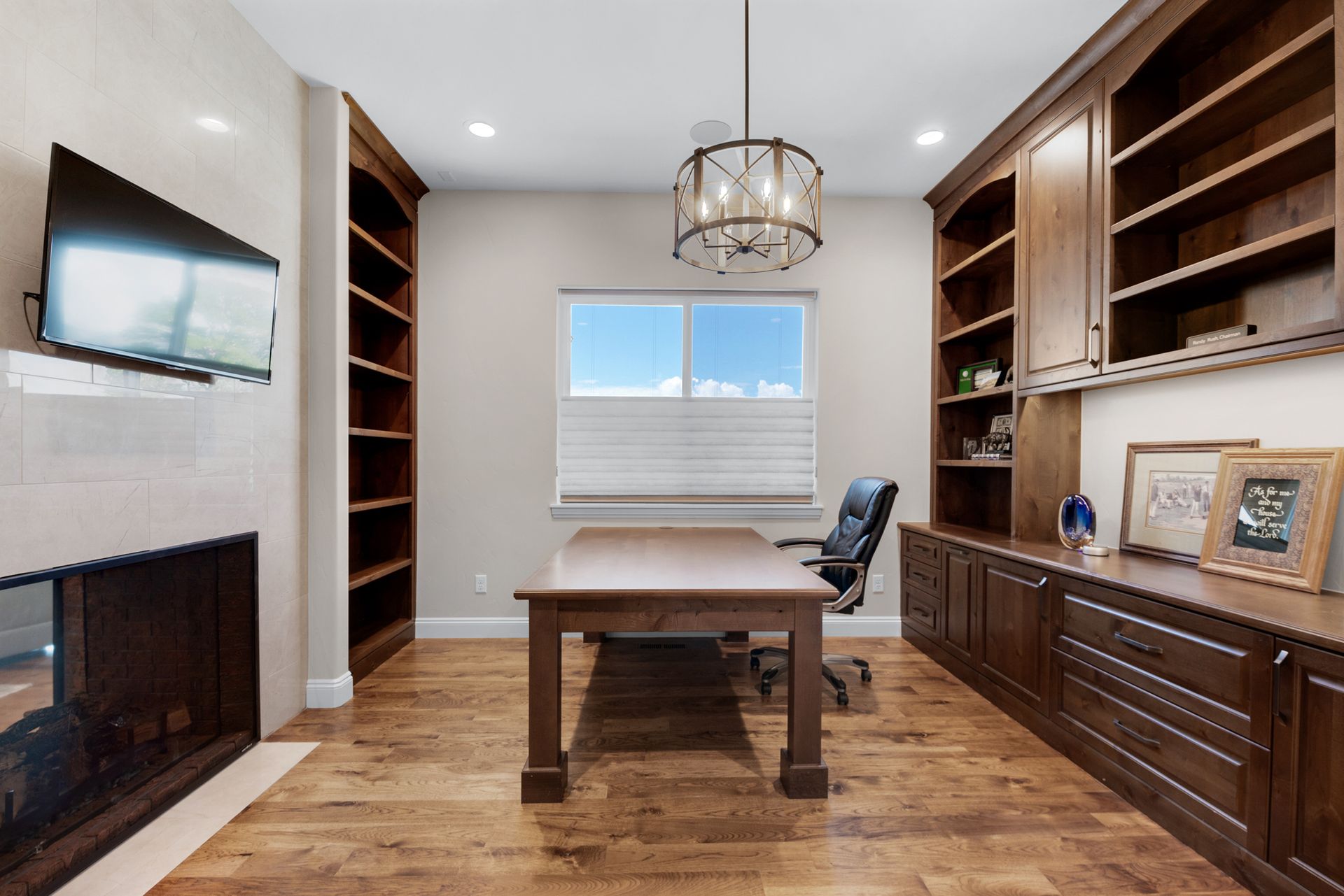 Home office with dark wood built-ins, desk, fireplace, TV, and a window.