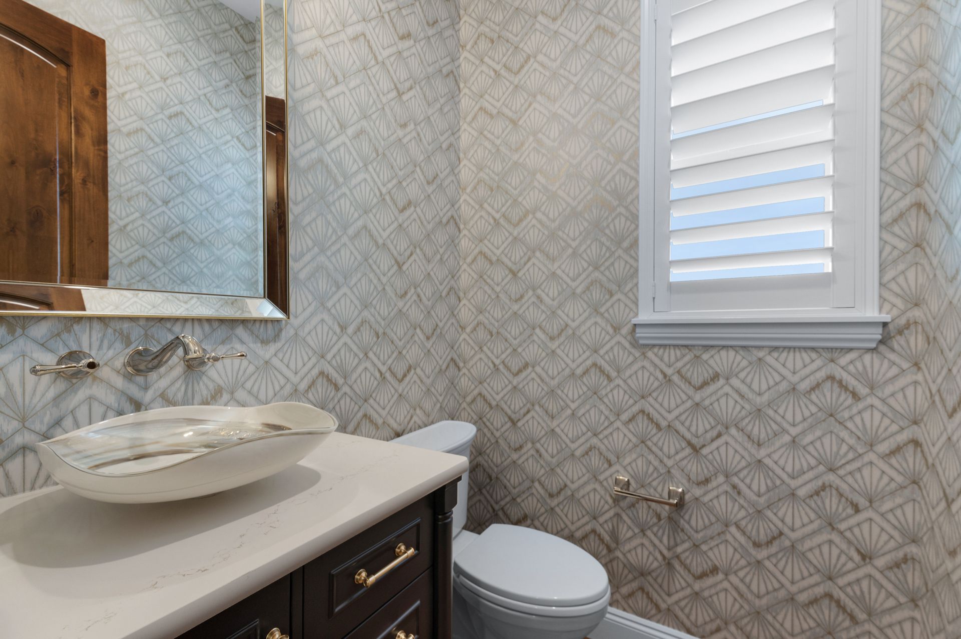 Powder room with patterned wallpaper, white toilet, sink, and shuttered window.