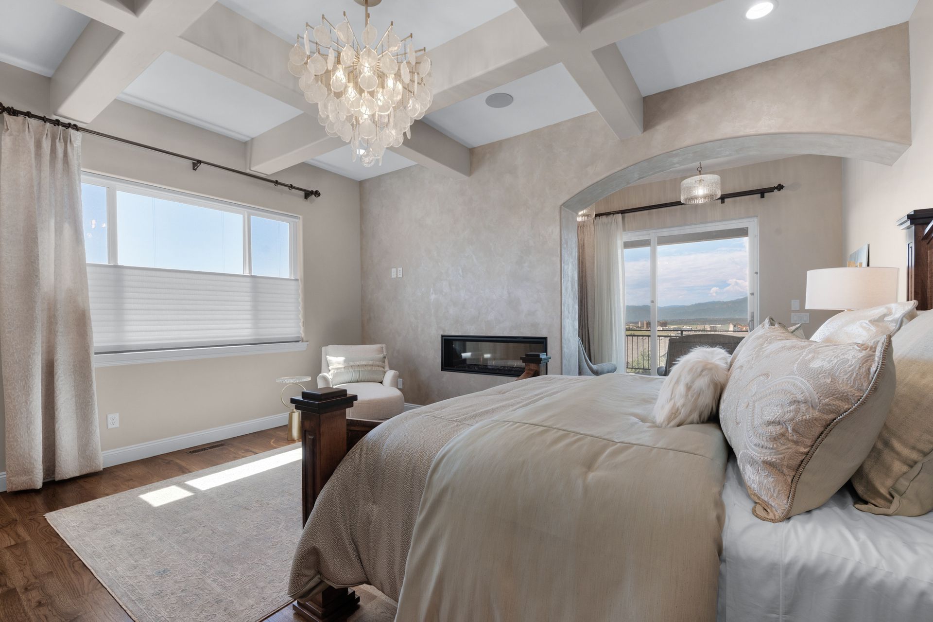 Bedroom with large bed, fireplace, windows, and decorative chandelier.