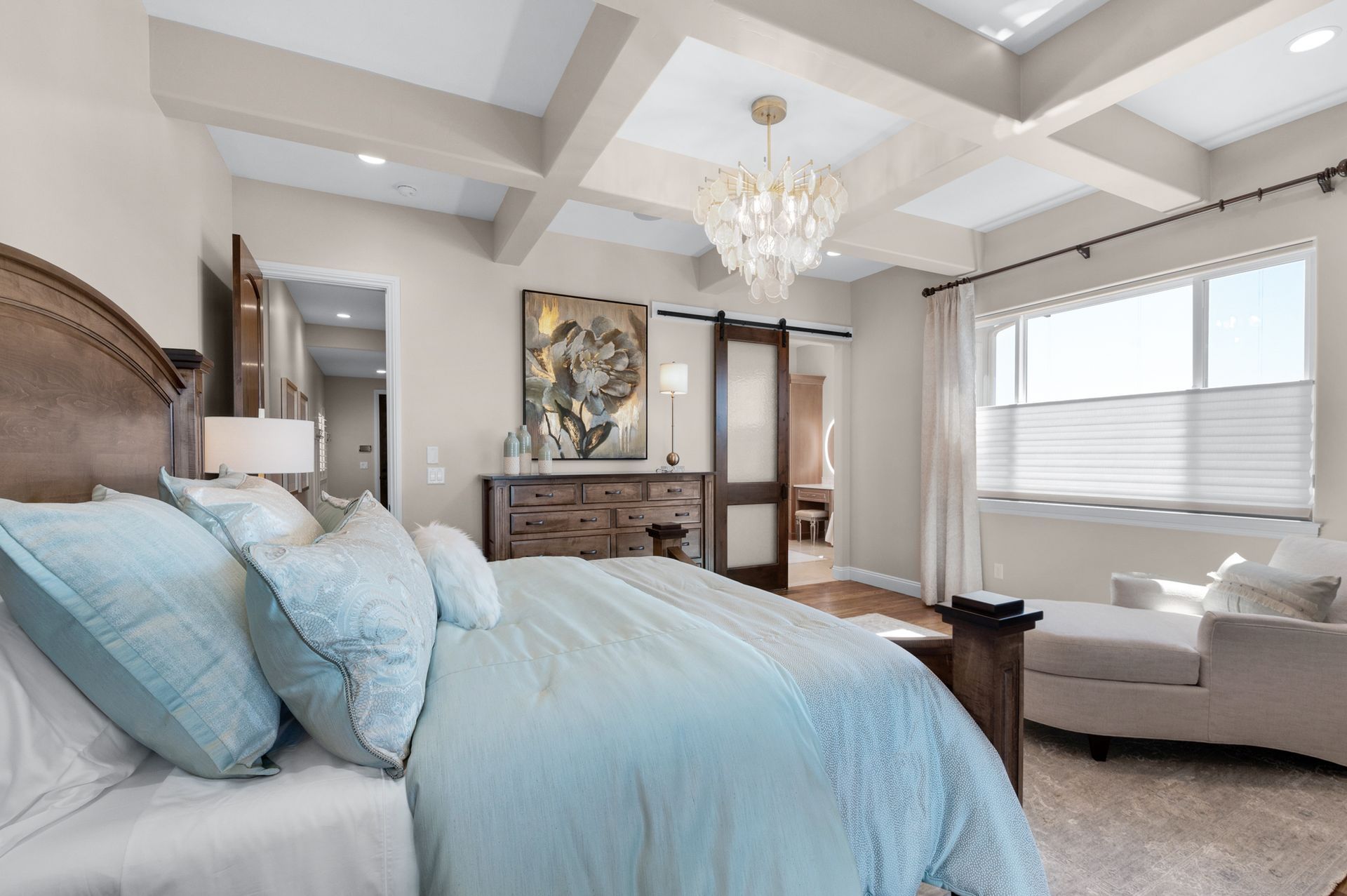 Bedroom with a large bed, chandelier, window, and a sitting area, in soft colors.
