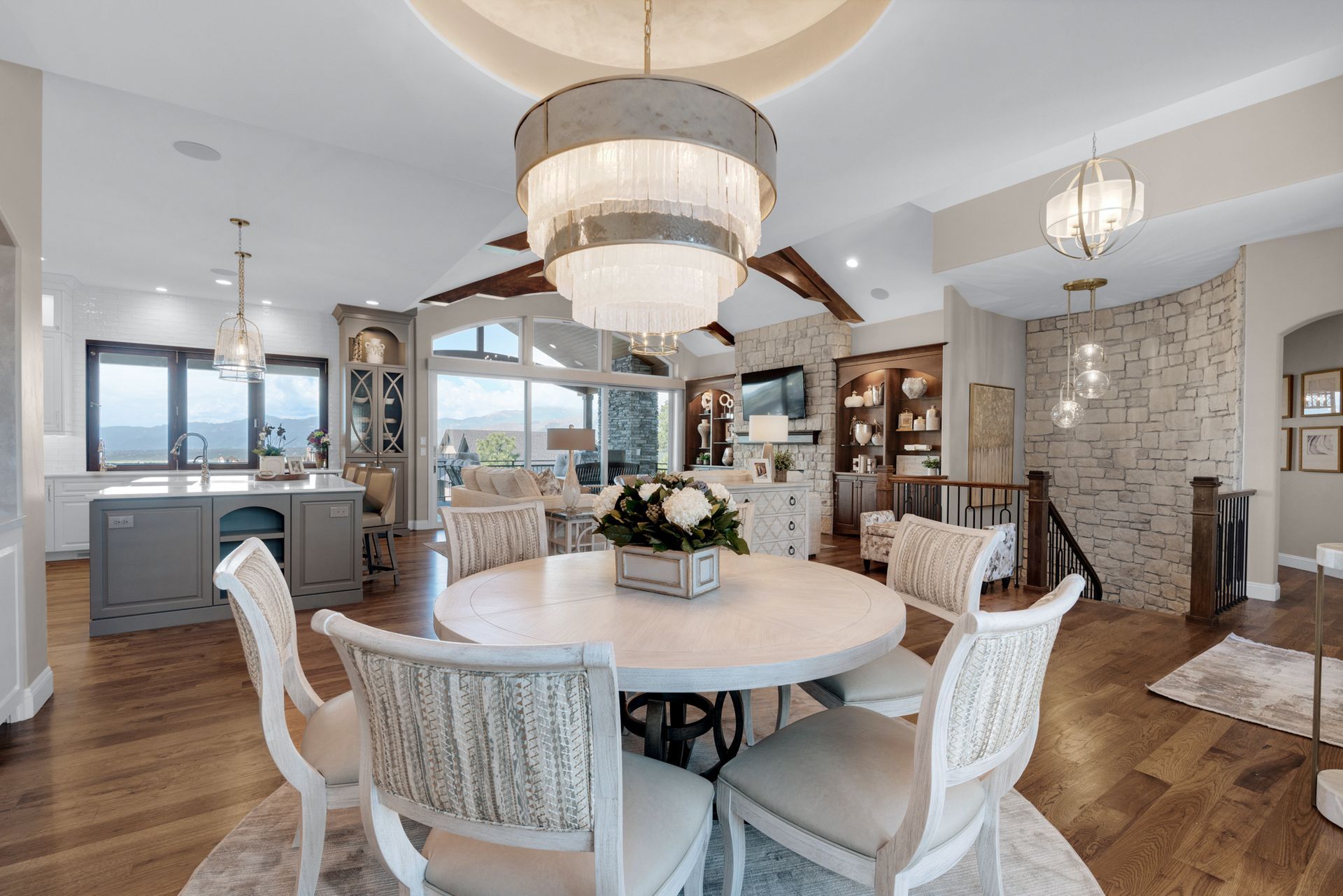 Dining room with white table and chairs, chandelier, open to kitchen with grey island, hardwood floors.