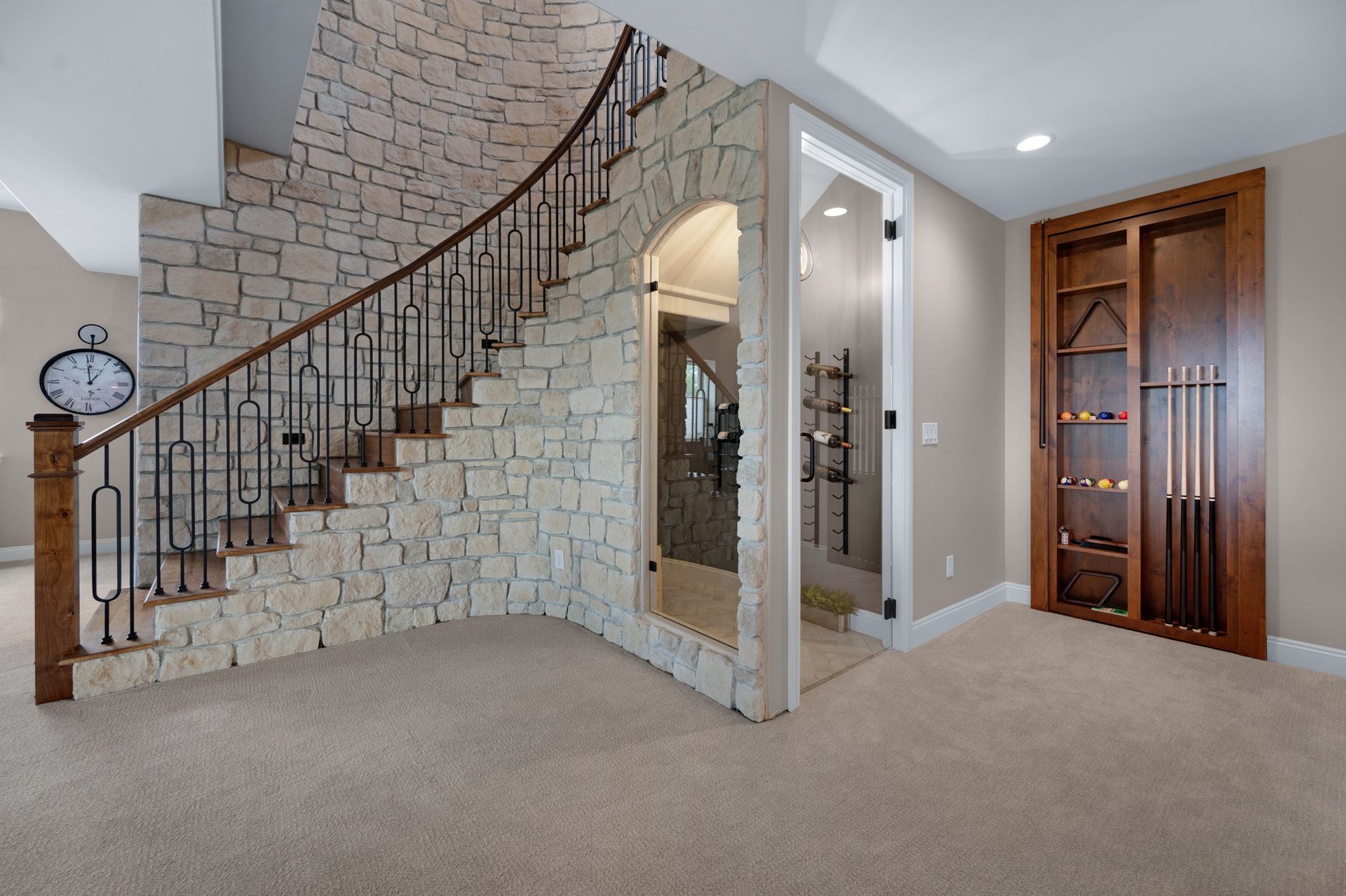 A stone-walled staircase, a wine cellar, and a pool cue cabinet in a room with beige carpet.