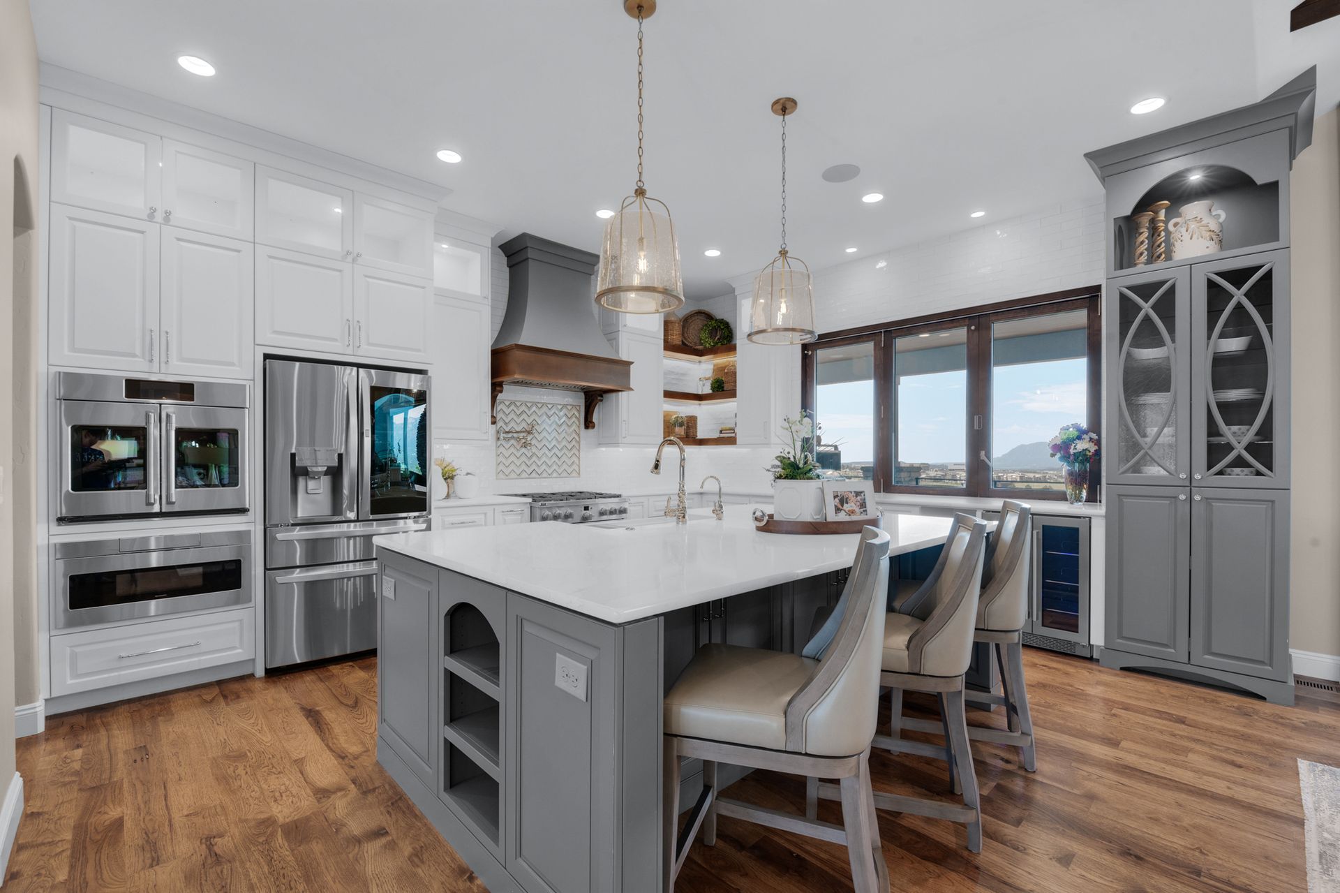 Spacious modern kitchen with white cabinets, gray island, stainless steel appliances, and pendant lights.