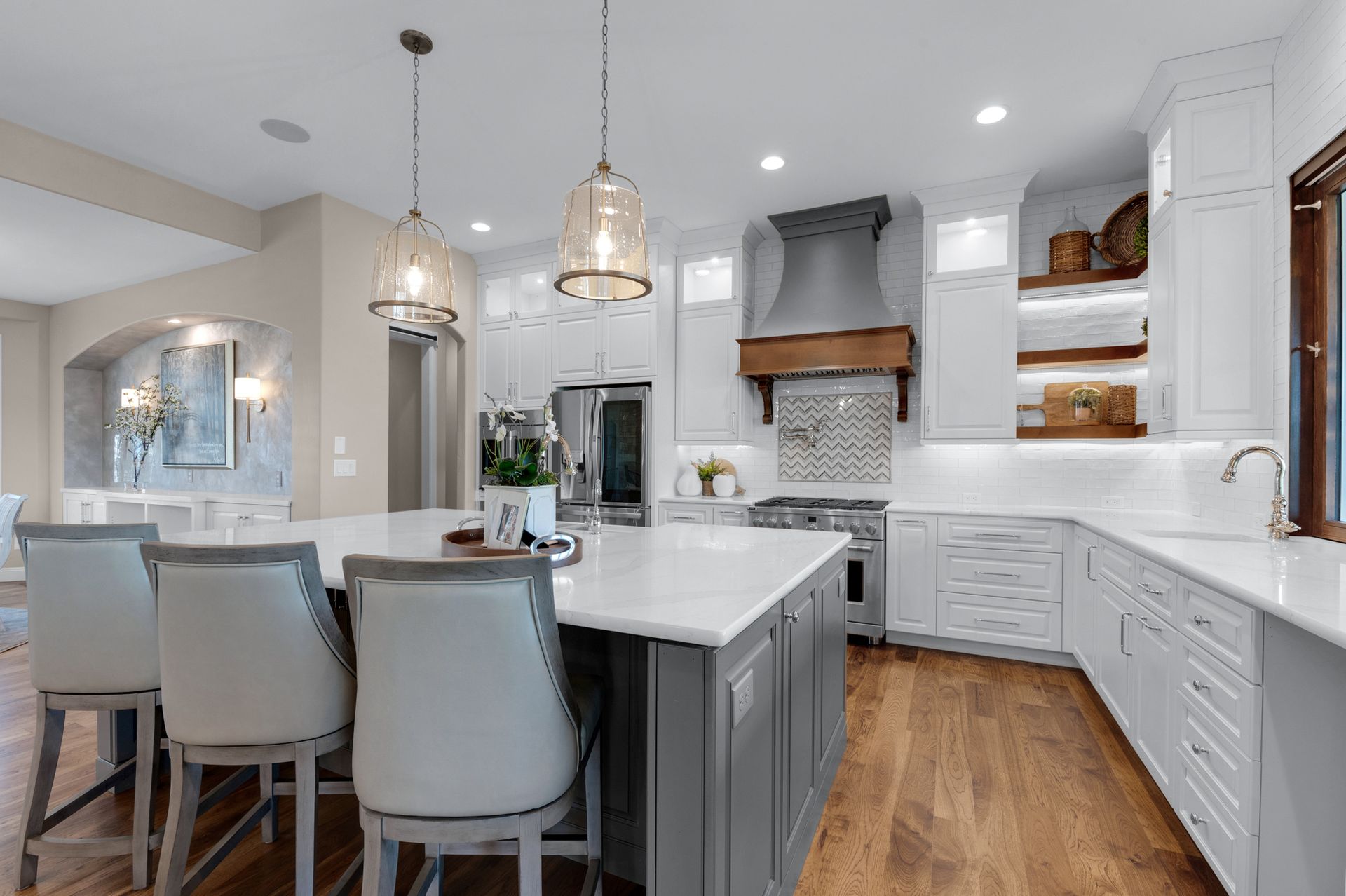Modern white kitchen with a gray island, wood floors, and three bar stools.