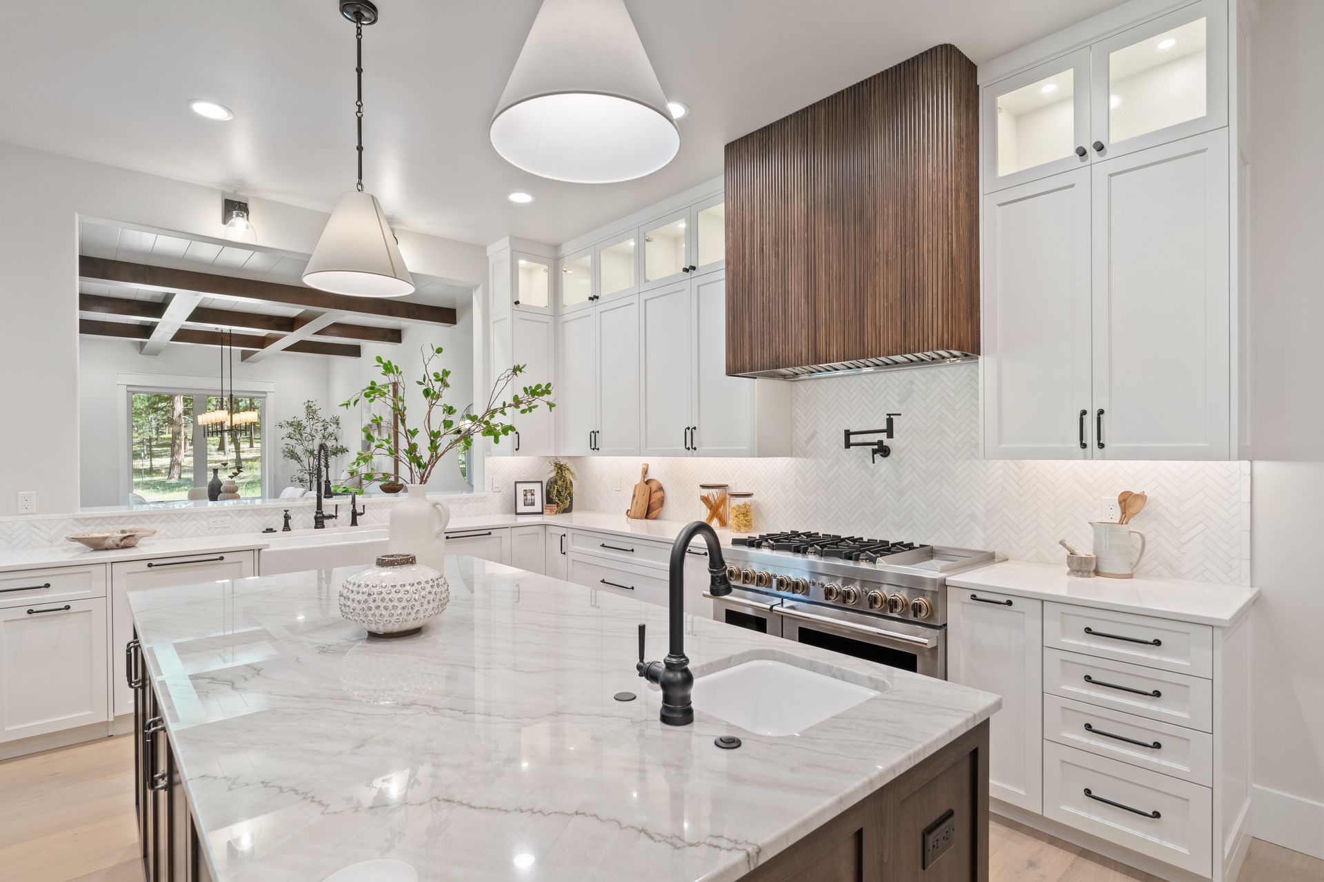 Modern kitchen with white cabinets, dark island, wood hood, and marble countertops.
