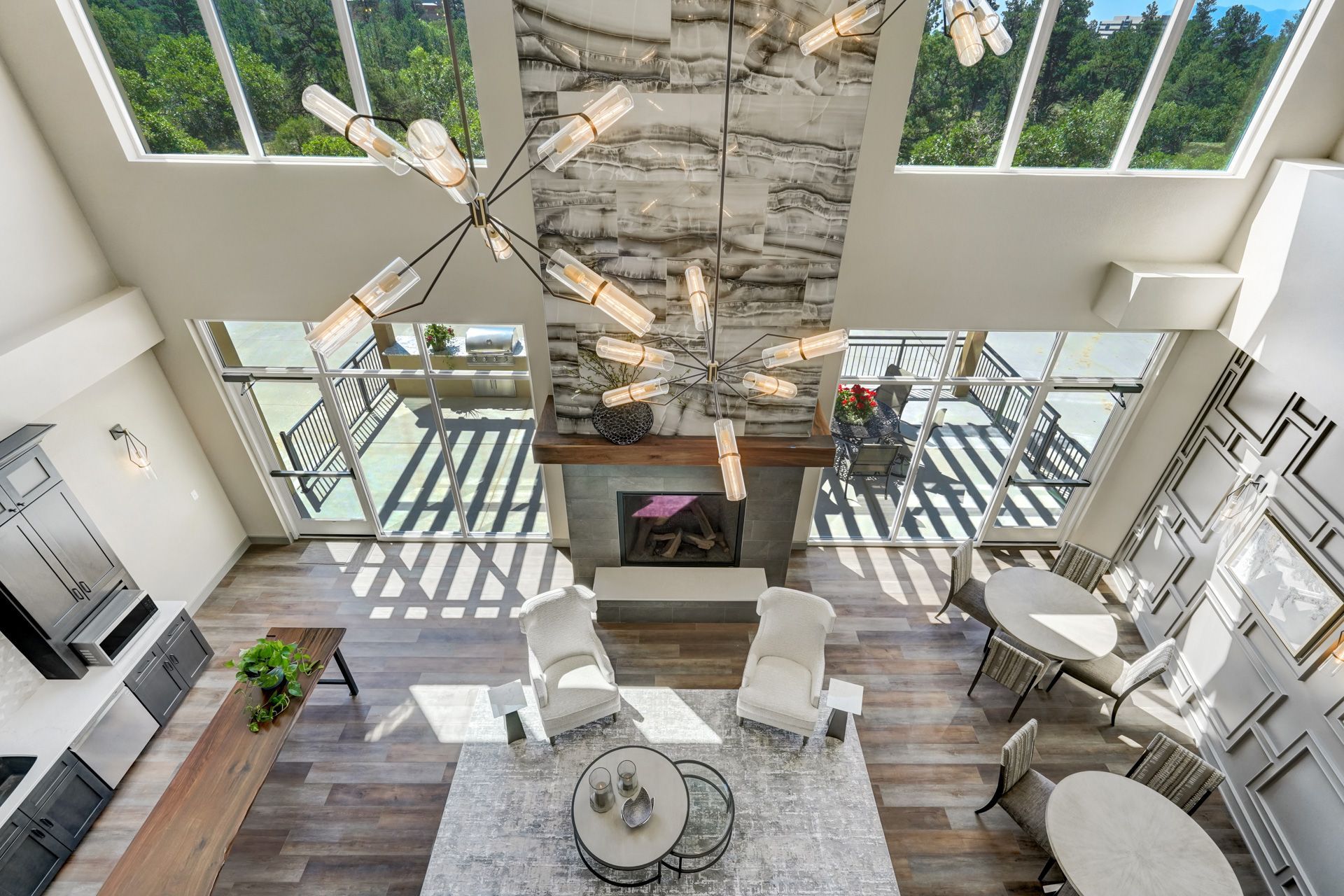 Modern interior with high ceilings, fireplace, chandelier, and large windows overlooking a forest.
