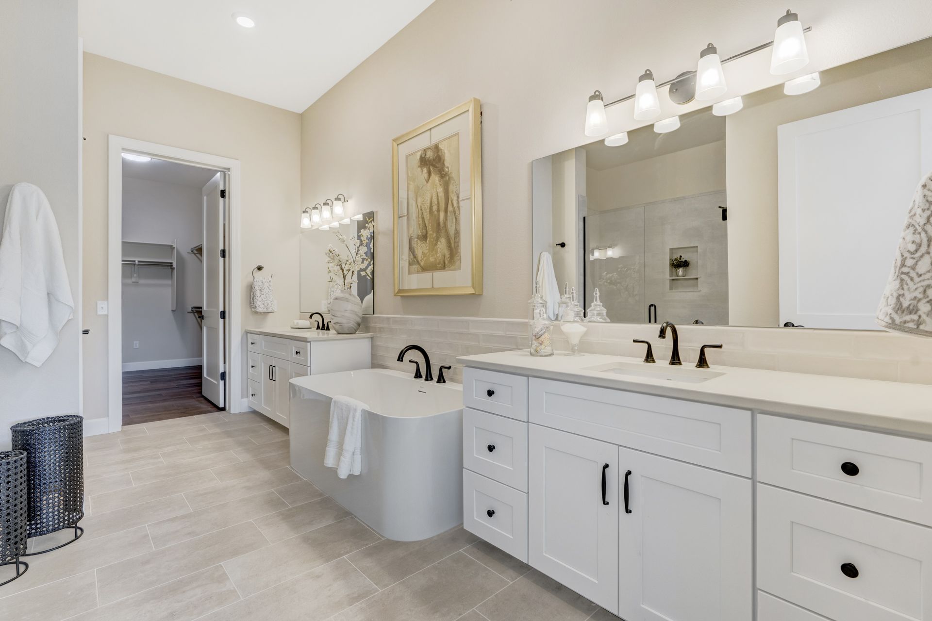 Spacious, modern bathroom with white cabinets, tub, and countertops, and light gray tile floor.
