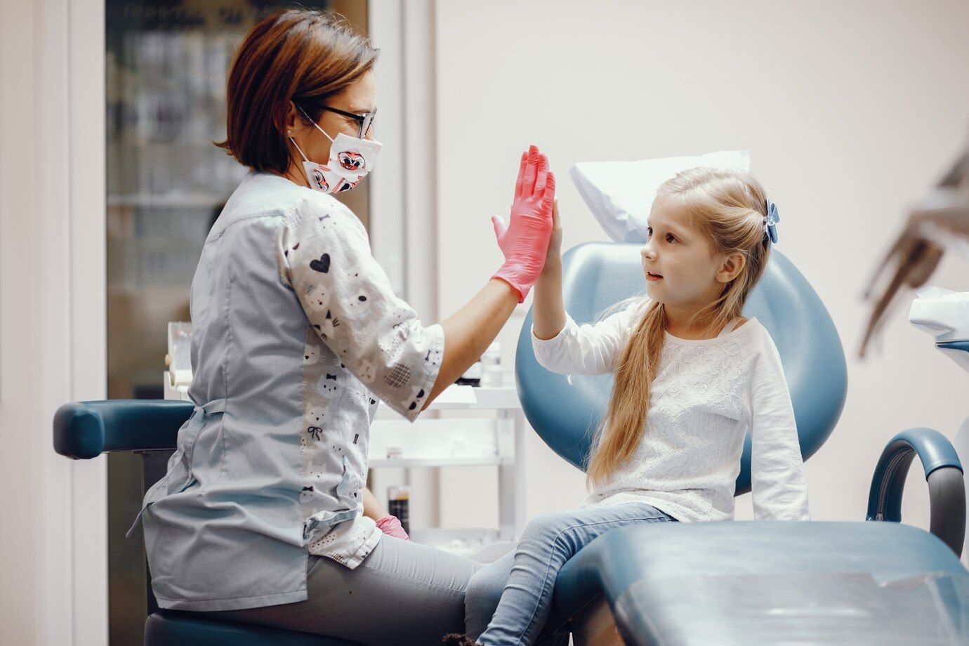 A little girl is giving a high five to a dentist in a dental office.