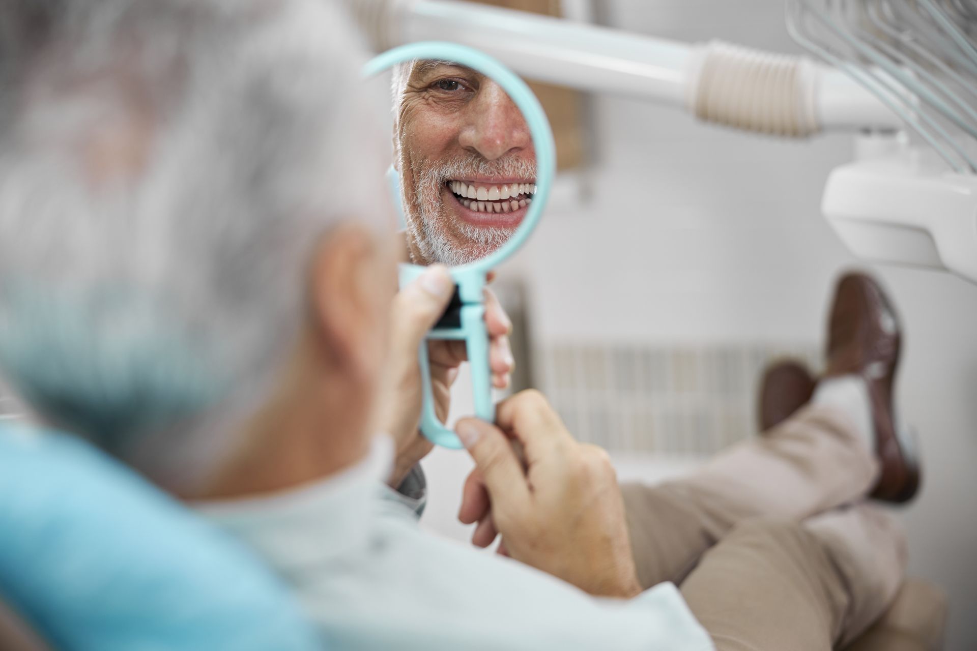 An older man is looking at his smile in a dental mirror.