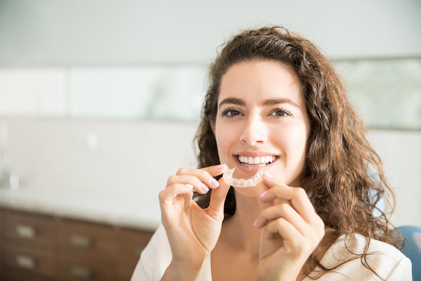 A woman is holding a clear brace in front of her mouth.