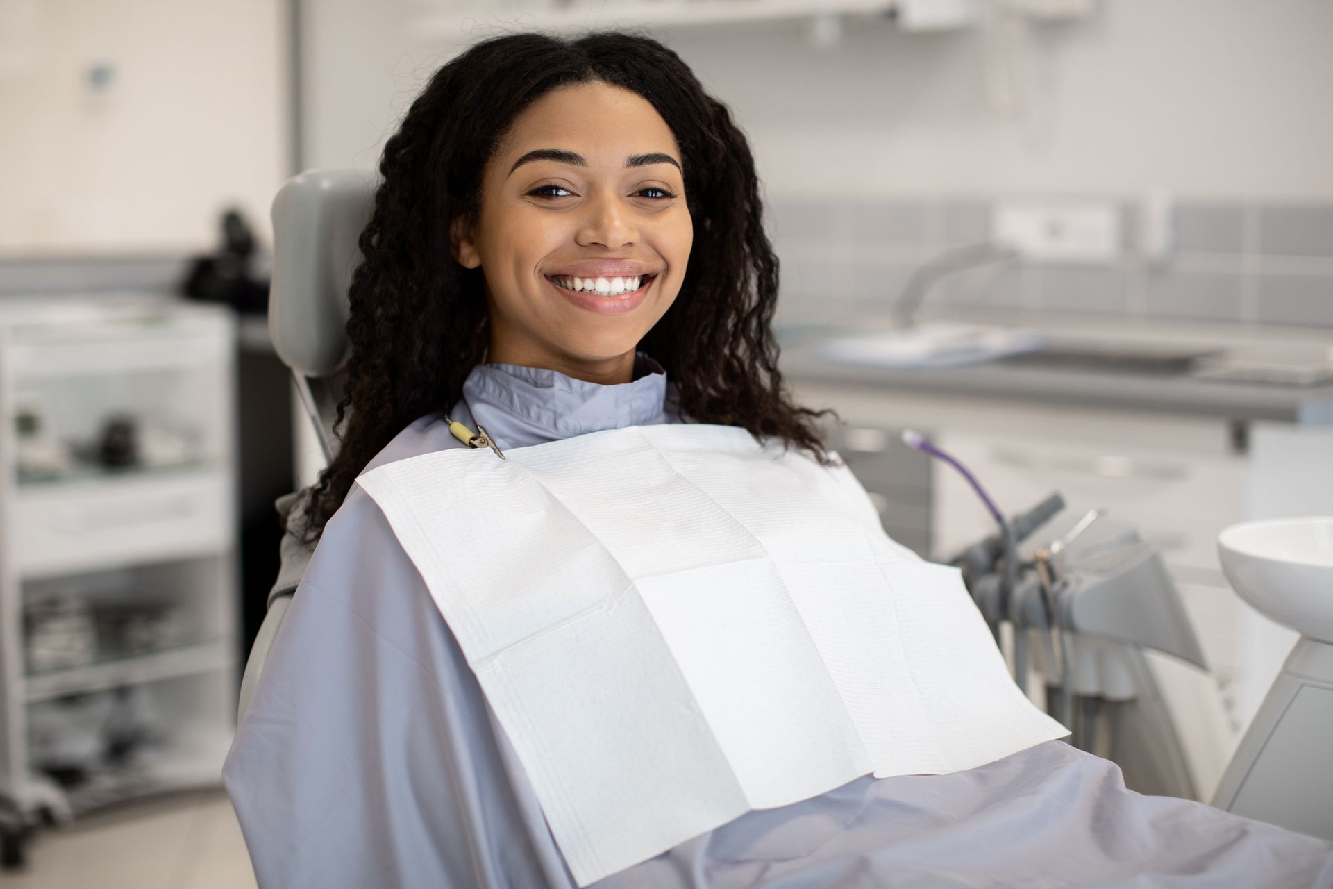 A woman is smiling while sitting in a dental chair.