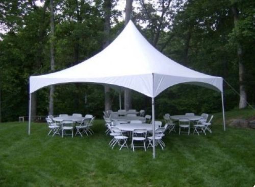 A white high-peak party tent set up on a grassy lawn with three round tables and white folding chairs underneath.