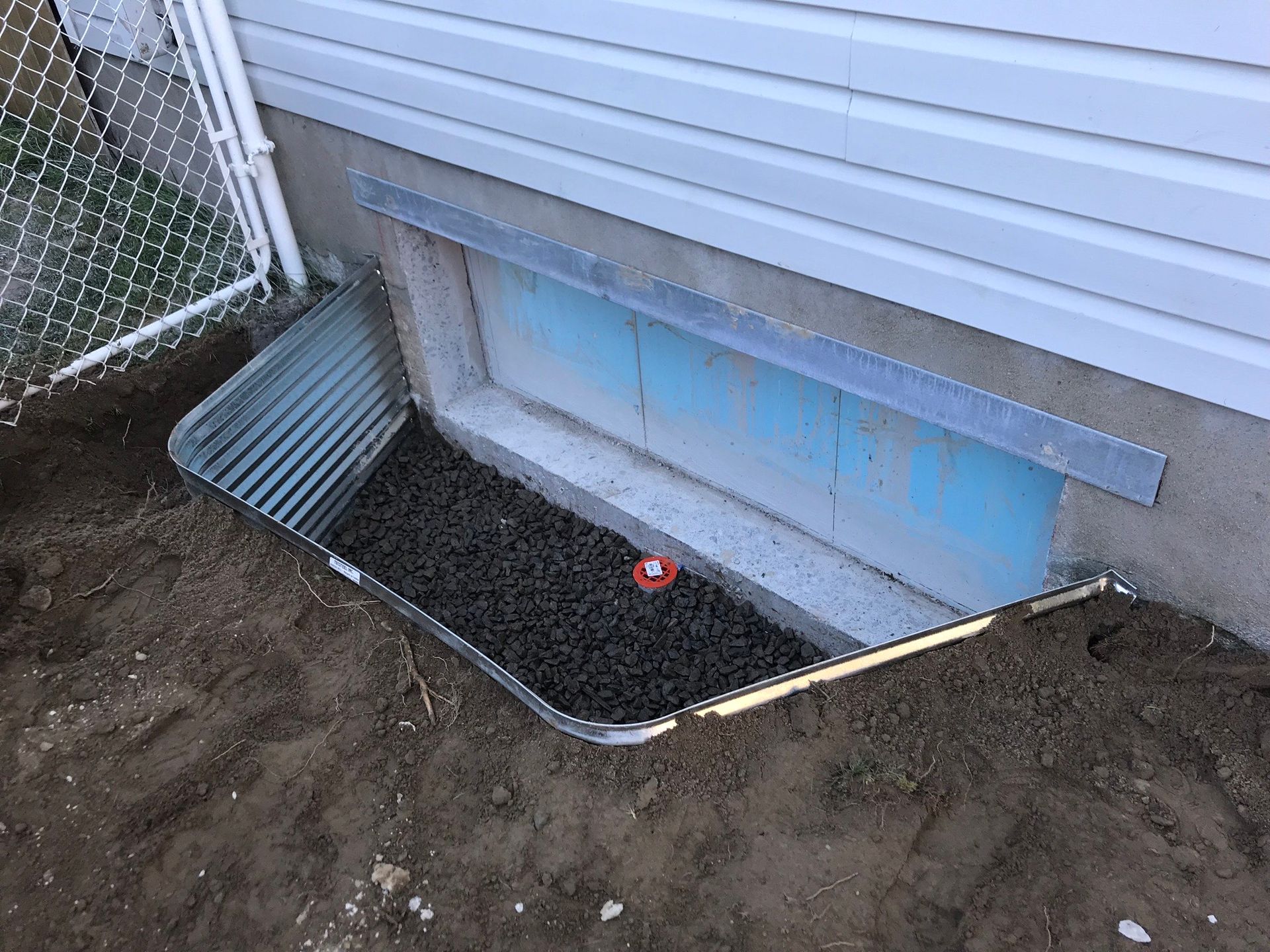 Une fenêtre bien enfoncée dans le sol à côté d'une maison.