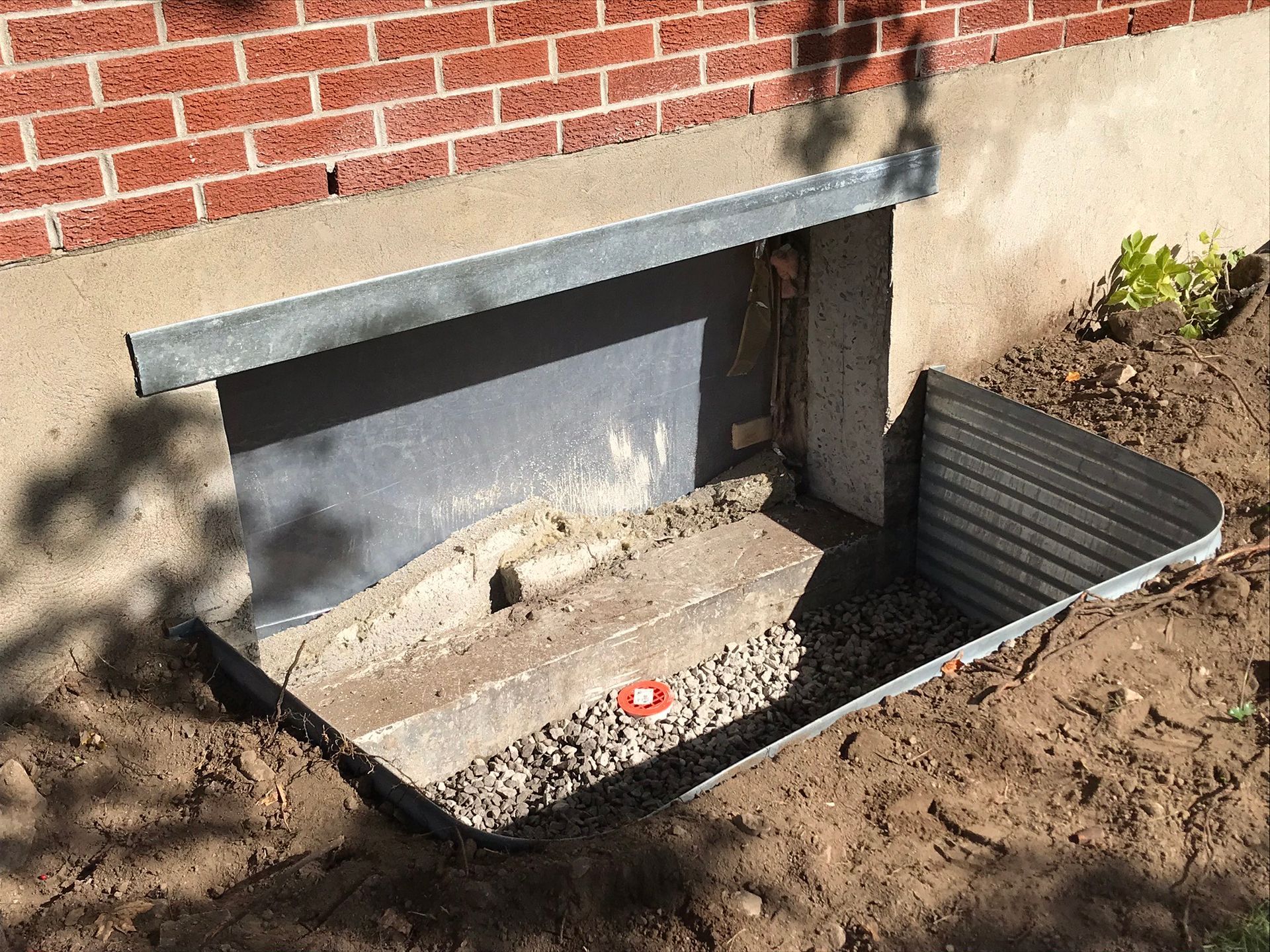 Une fenêtre bien enfoncée dans le sol à côté d'un bâtiment en brique.
