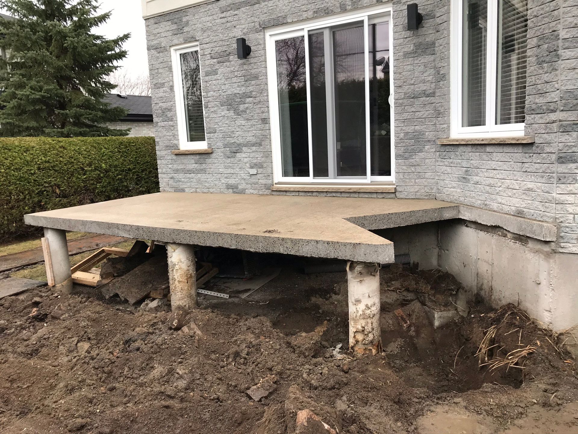 Une terrasse en béton est en cours de construction devant une maison en brique.