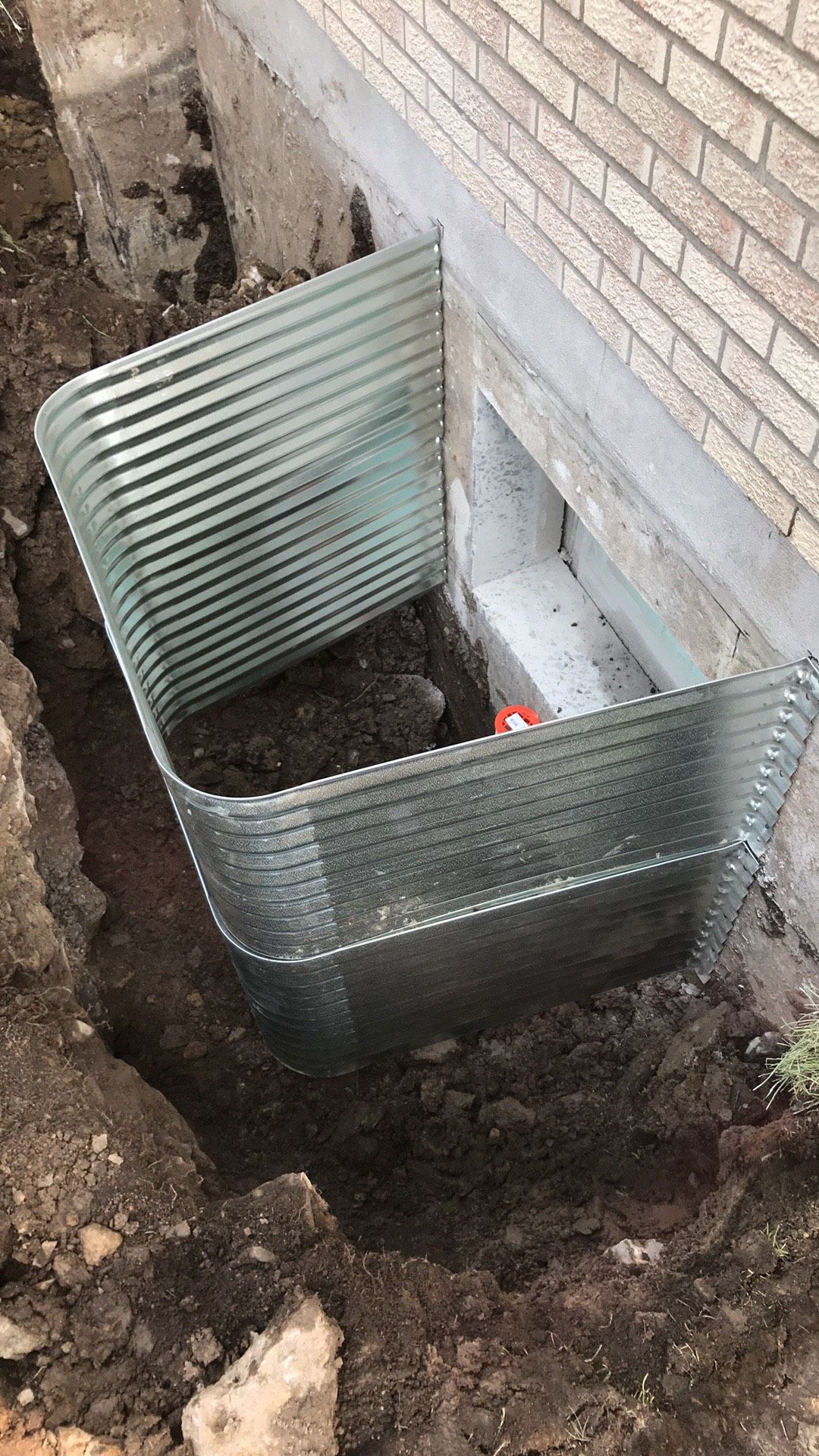 Une fenêtre bien enfoncée dans le sol à côté d'un mur de briques.