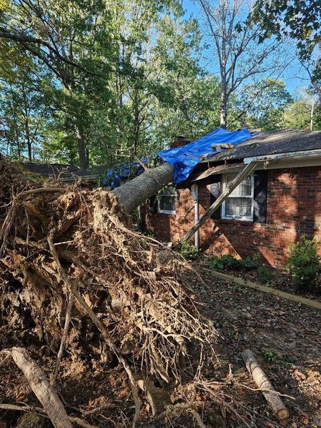 Single-story brick house with a porch, large leafless tree, and a red crane truck in the yard under a blue sky