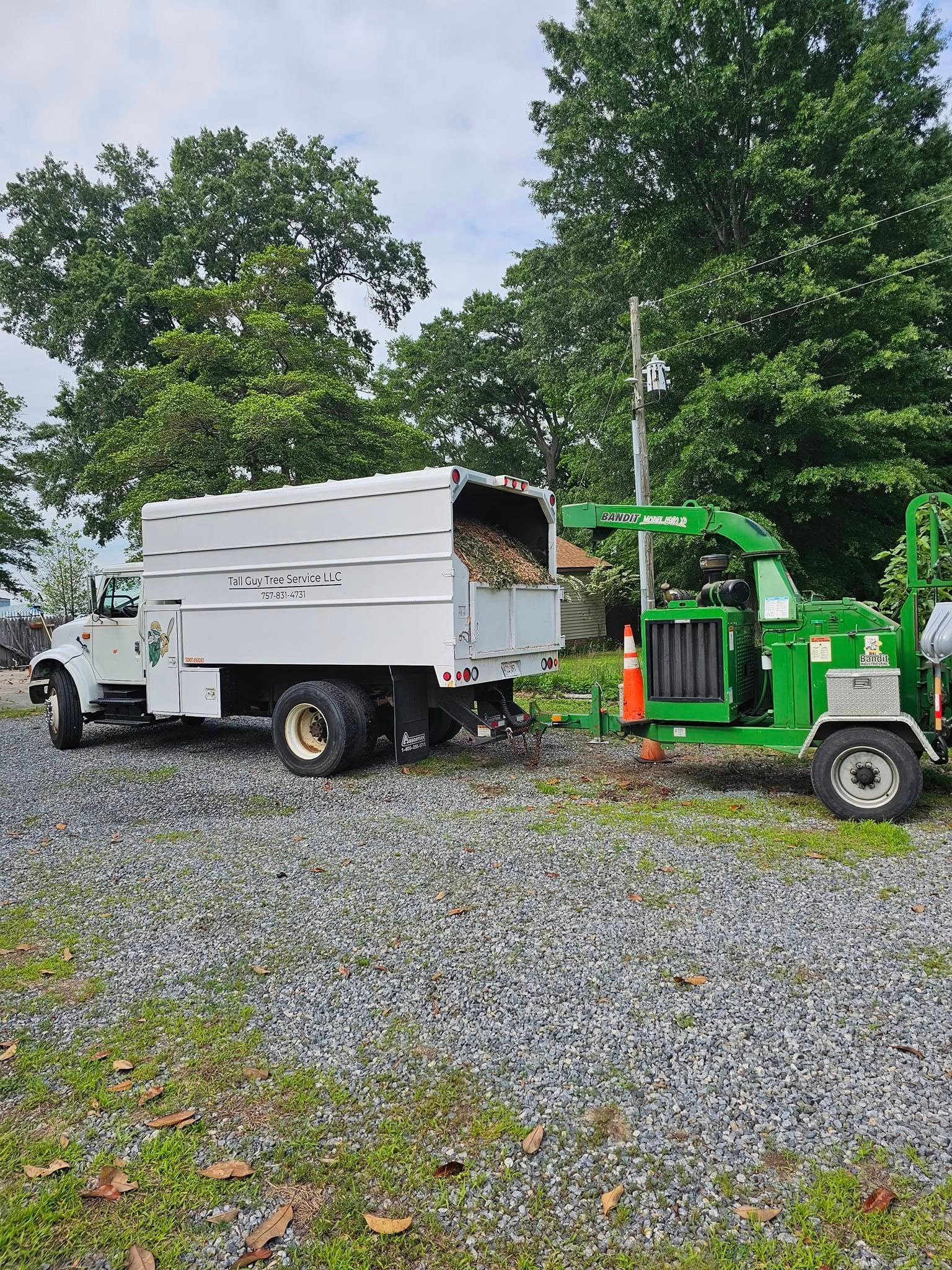 Green forklift unloading a white truck on a gravel lot with trees in the background