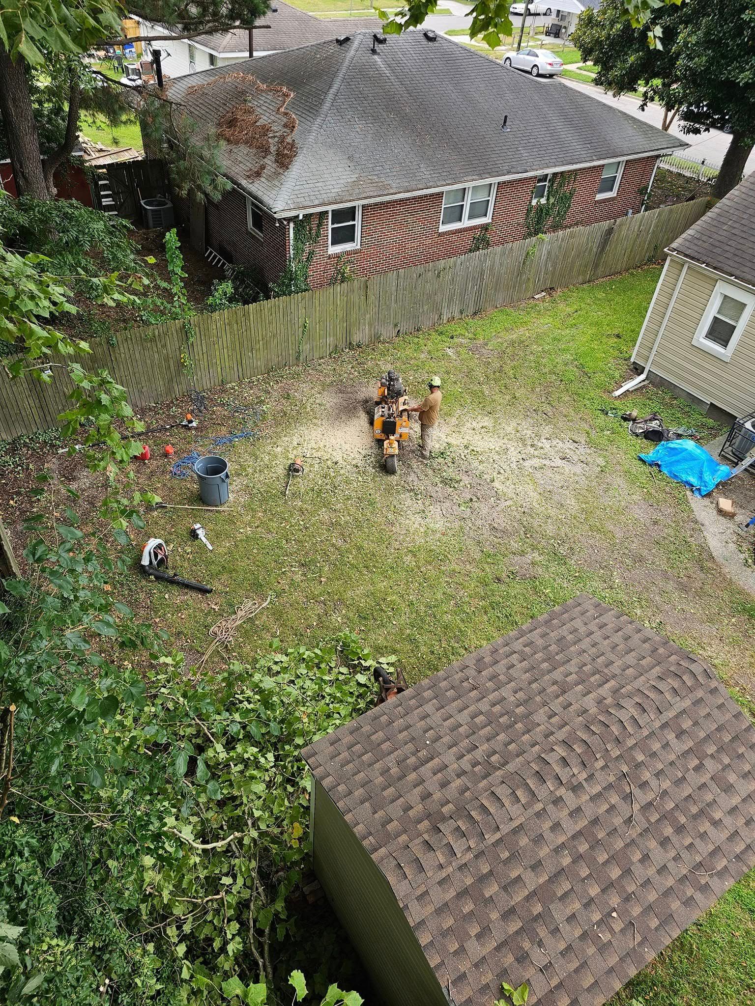 Backyard with scattered leaves, two people near a small fire pit, and neighboring houses and sheds around it
