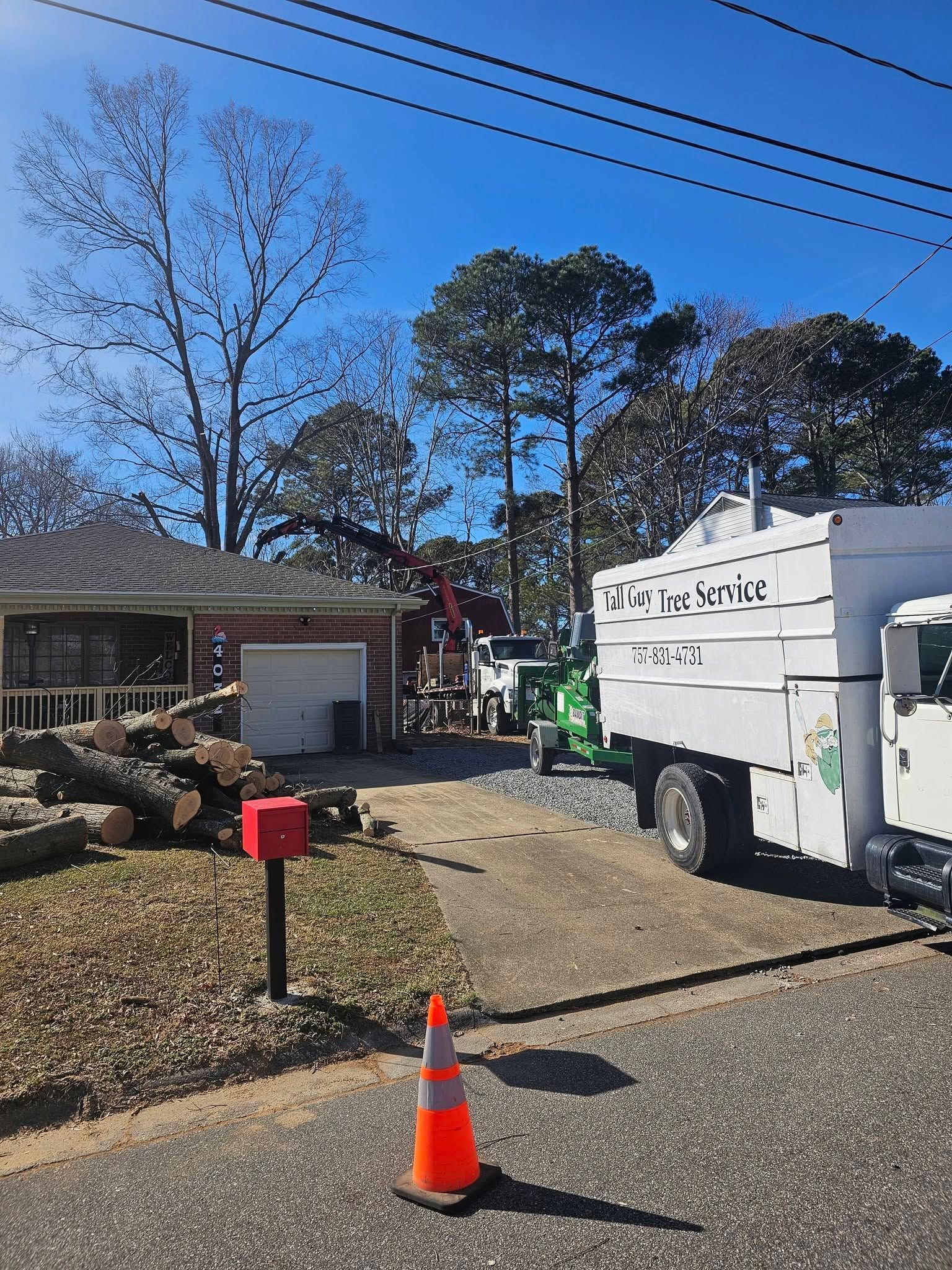 Utility truck and worker on a residential street, with traffic cones and a house in the background.