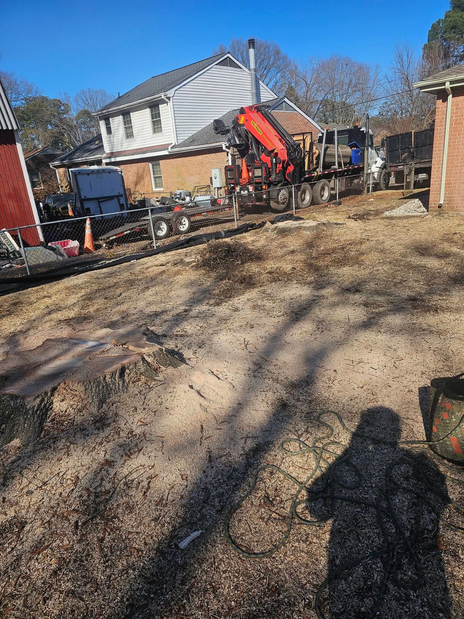 Construction equipment in a muddy yard beside a house, with an orange excavator and trucks under a blue sky.