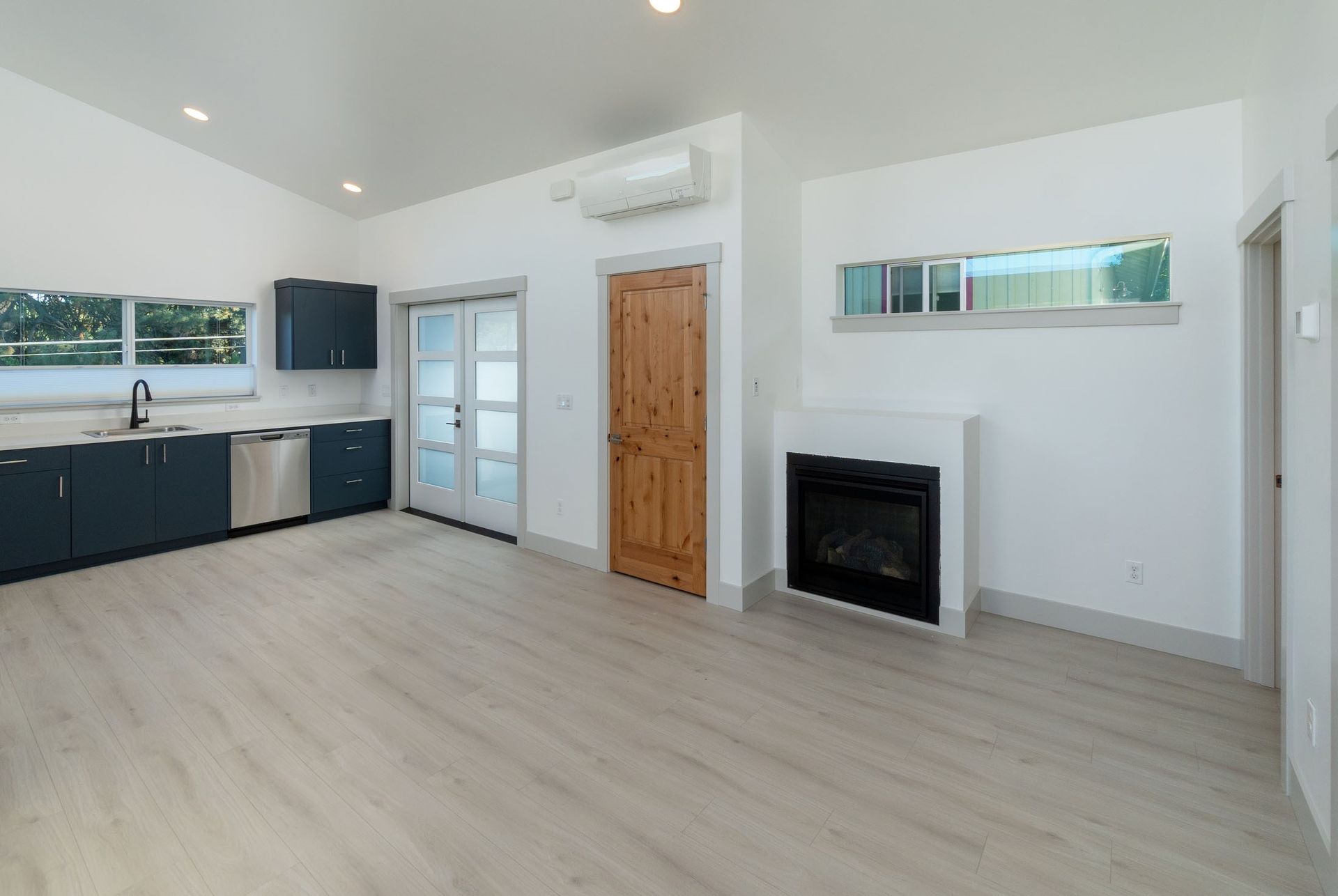 An empty living room with a fireplace and a kitchen.