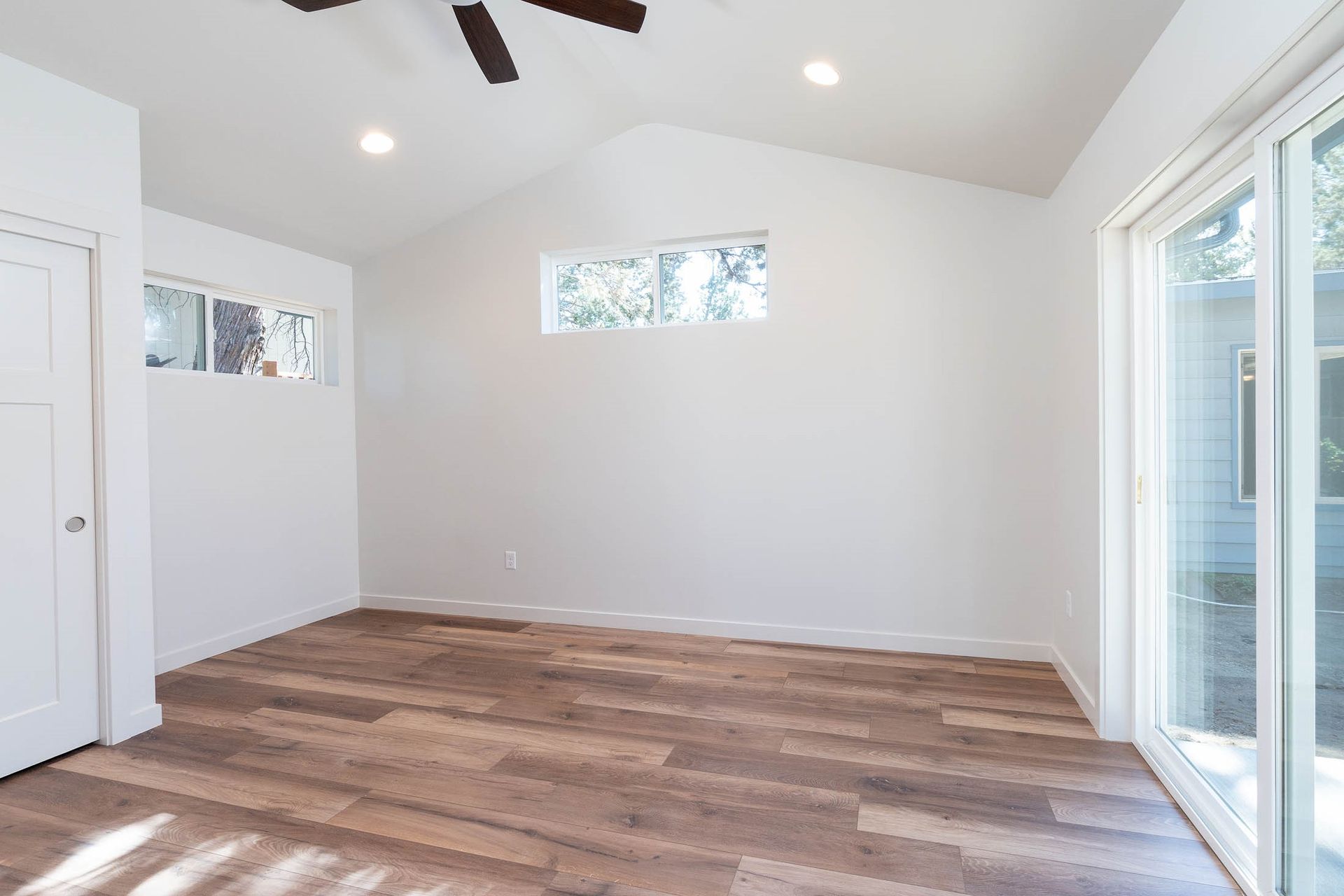 An empty room with a ceiling fan and sliding glass doors.
